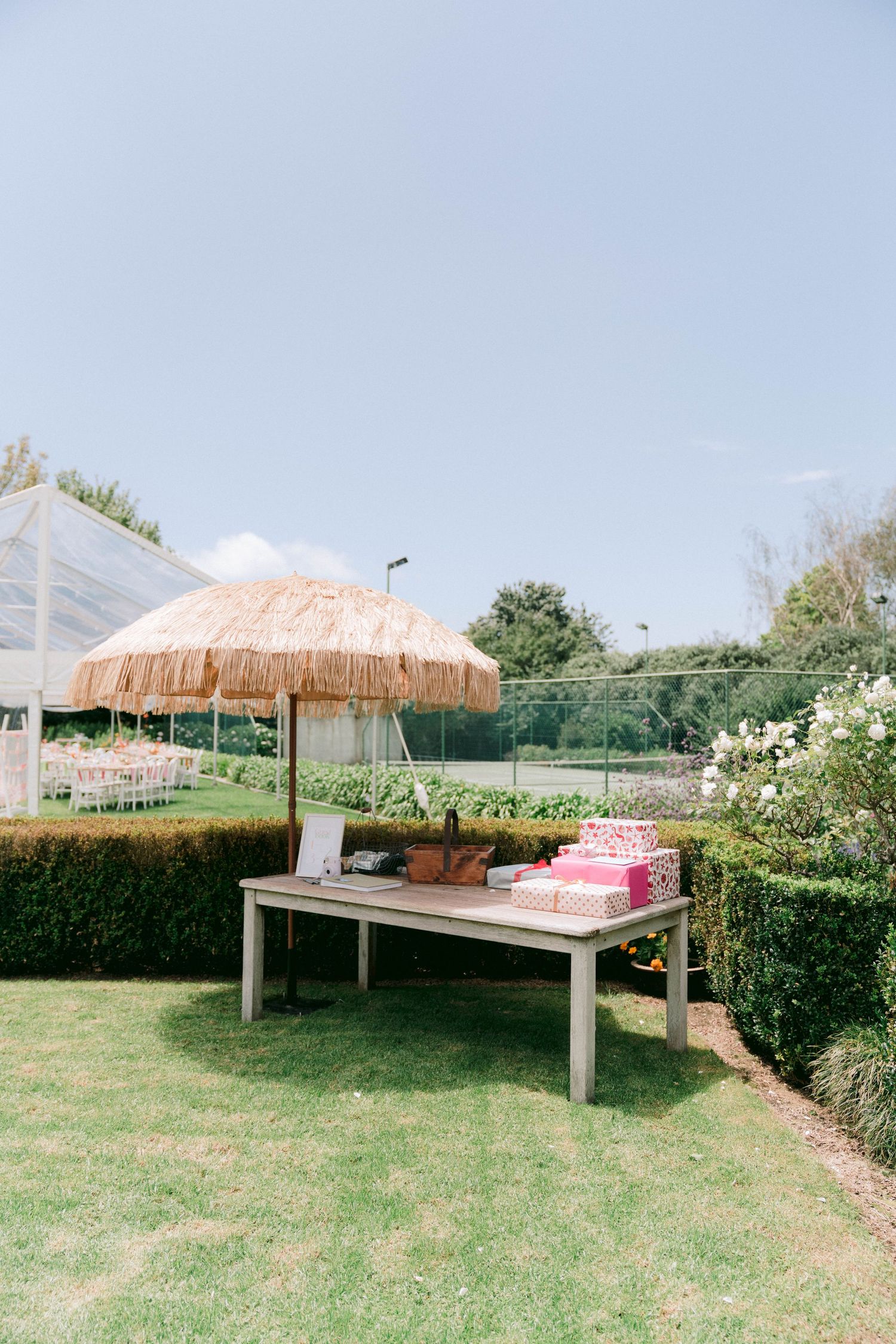 Outdoor wedding reception setup with thatched umbrellas and tables on a grassy lawn.