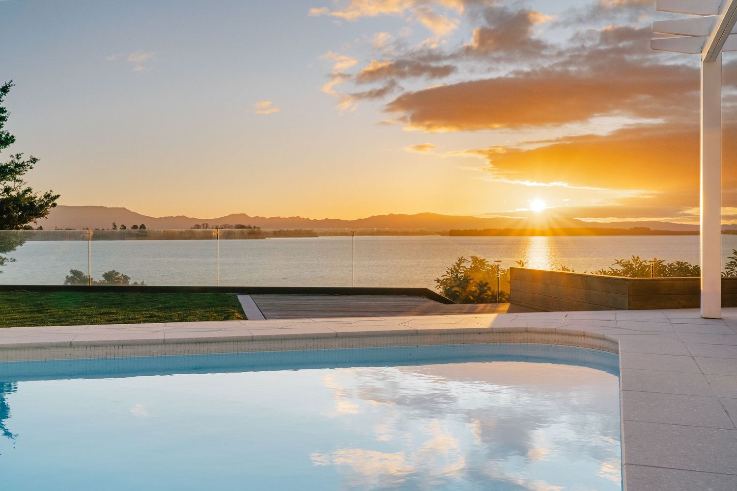 Modern infinity pool reflecting golden sunset over waterfront landscape.