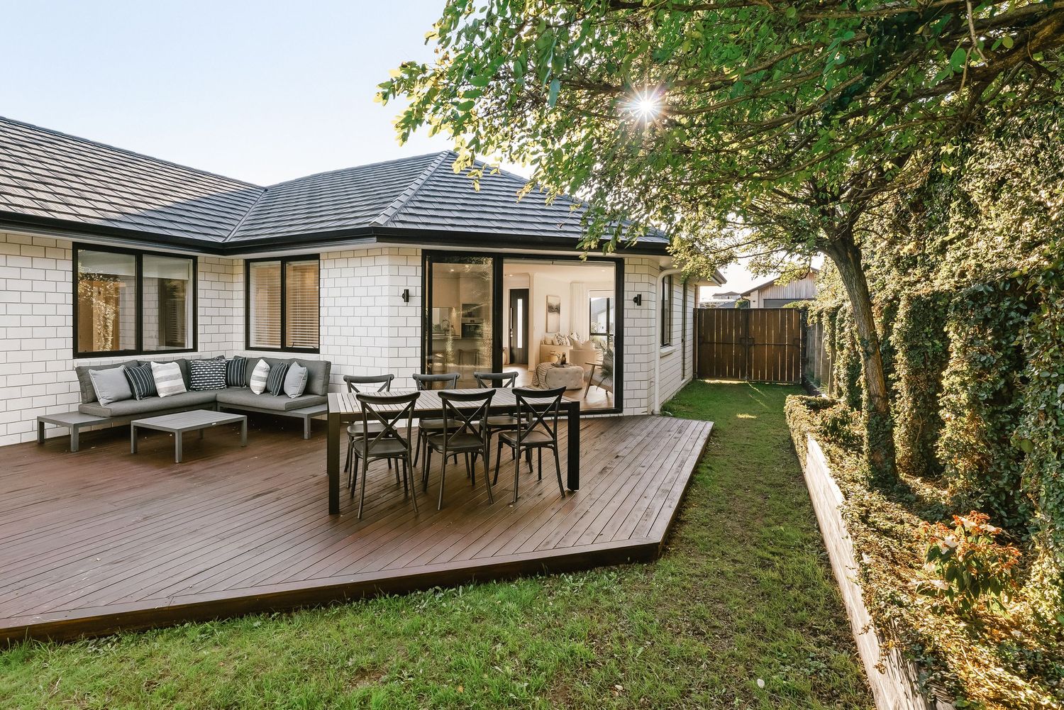 Contemporary home exterior with spacious wooden deck featuring outdoor dining and lounge furniture.
