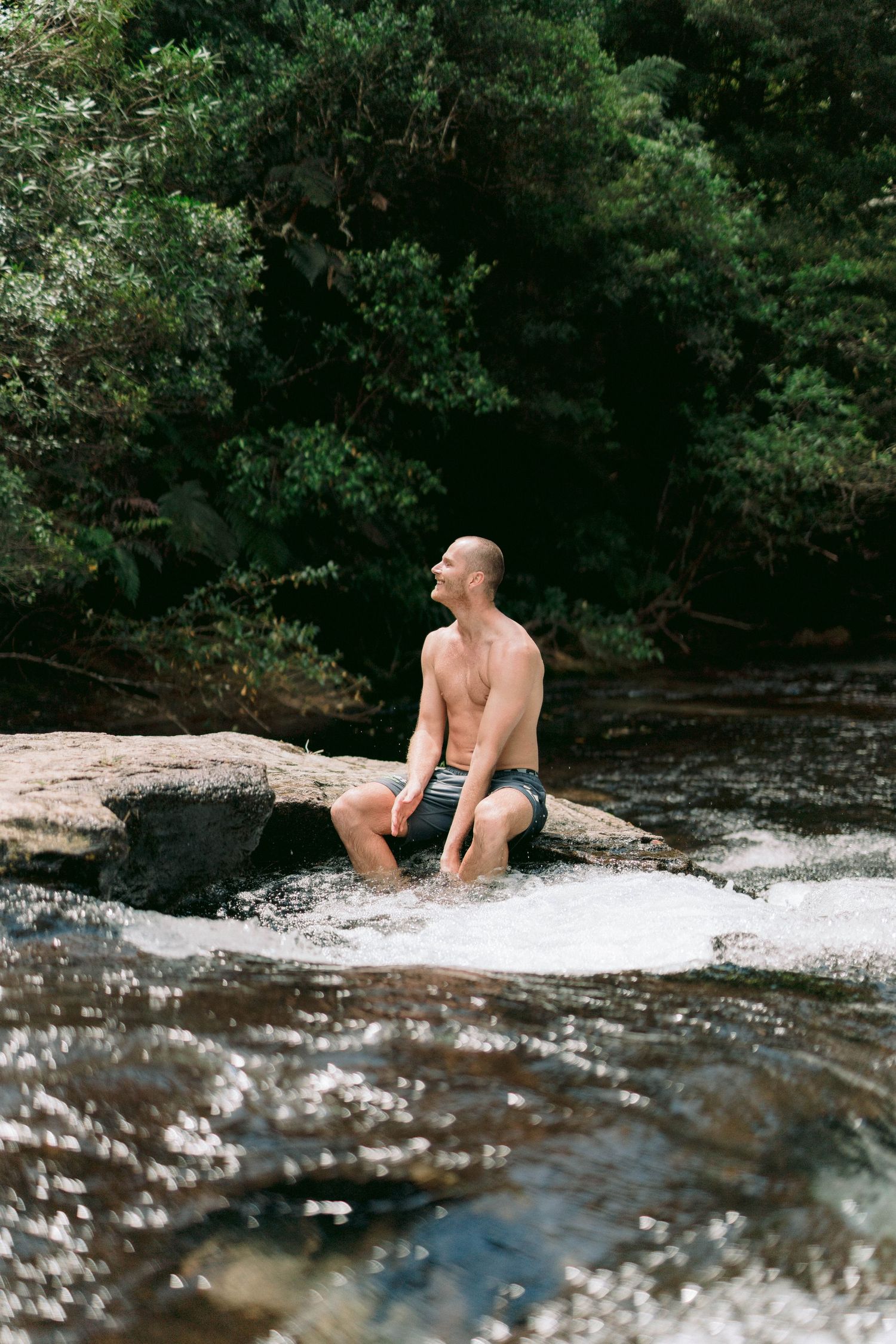 Person relaxing on rocks by cascading waterfall in a scenic forest setting.