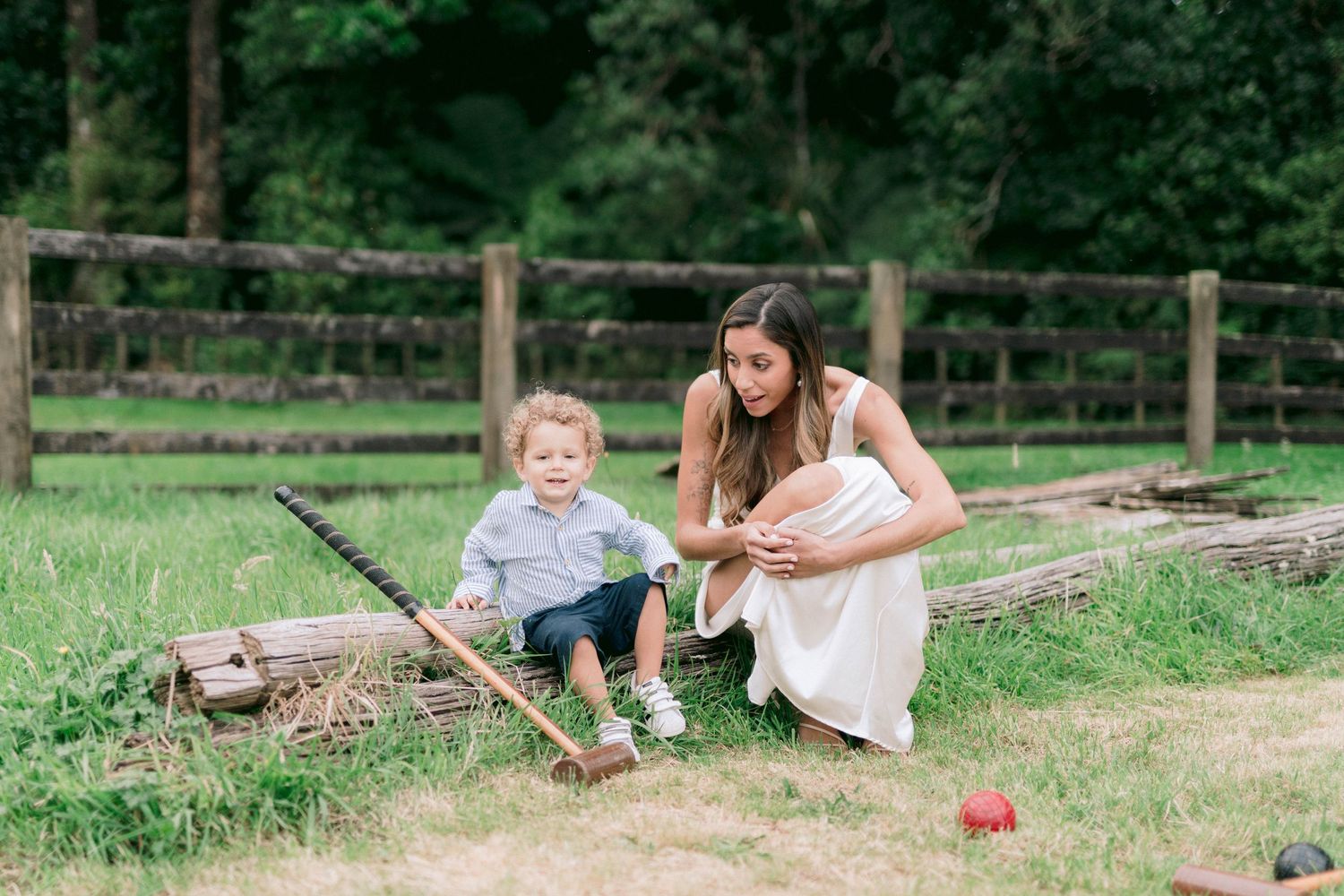Children play and swing in a rustic outdoor garden setting with wooden fencing.