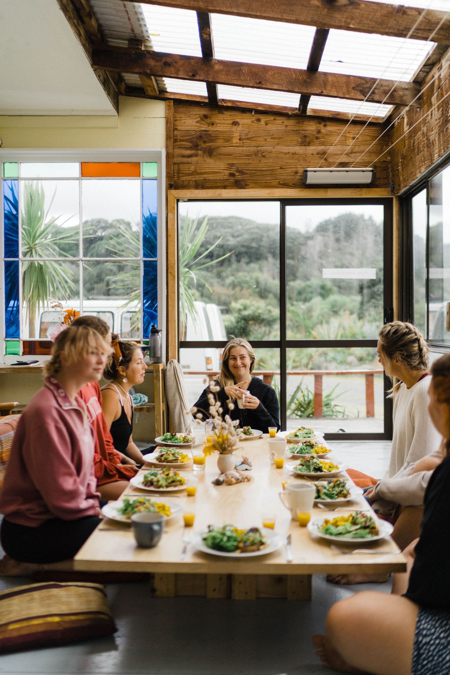 Group enjoying lunch together at wooden table with mountain views through large windows.