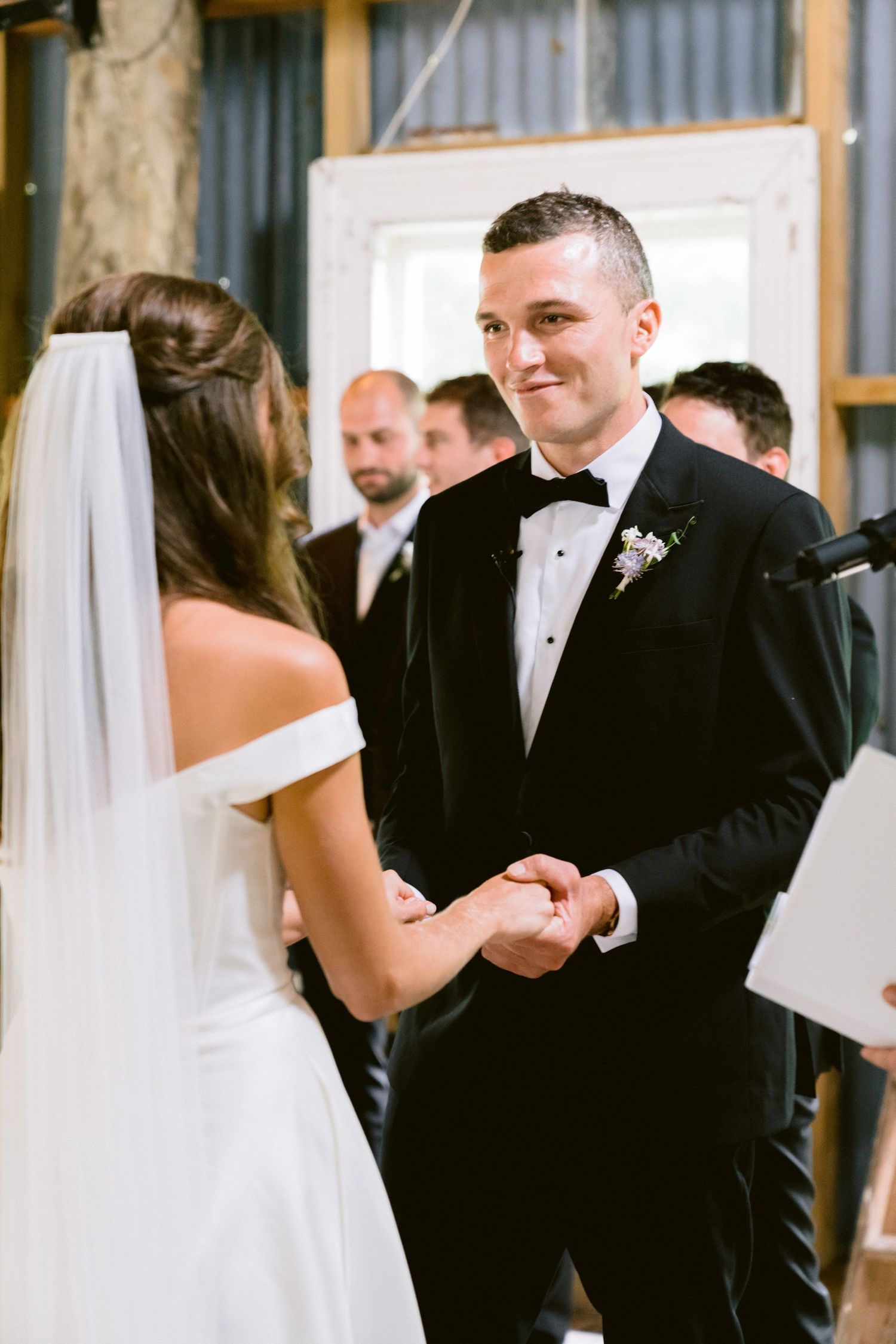 A couple exchanges vows during their wedding ceremony with the groom in a classic black tuxedo.