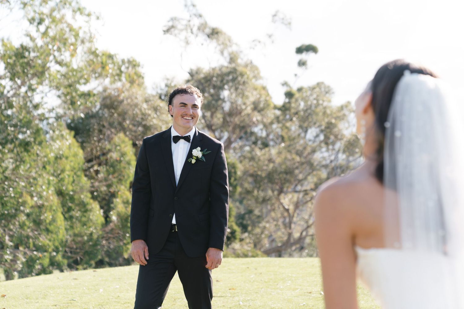 First look moment between bride and groom on sunny hilltop.