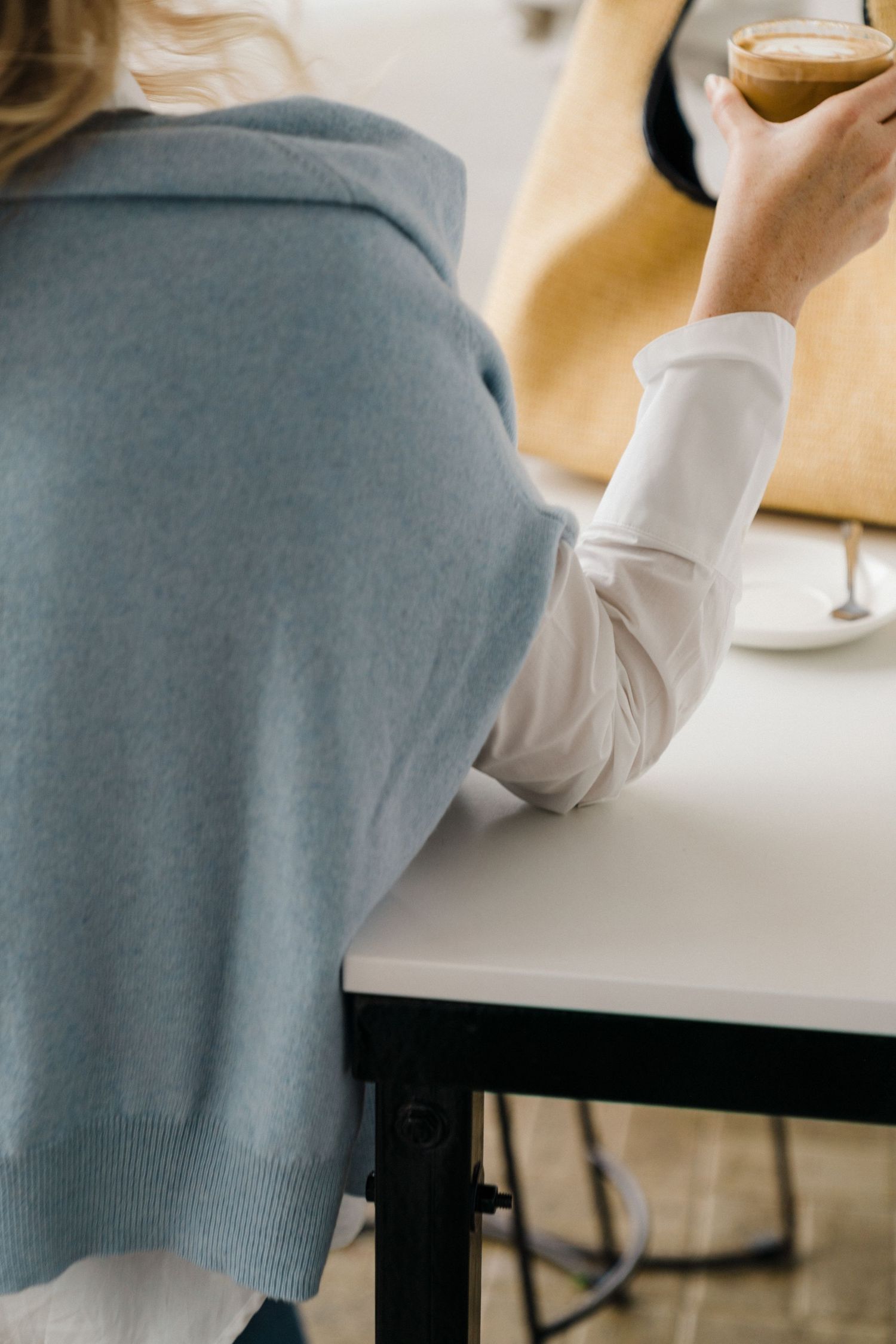 Person in grey sweater and white shirt holding a cocktail glass at a table.