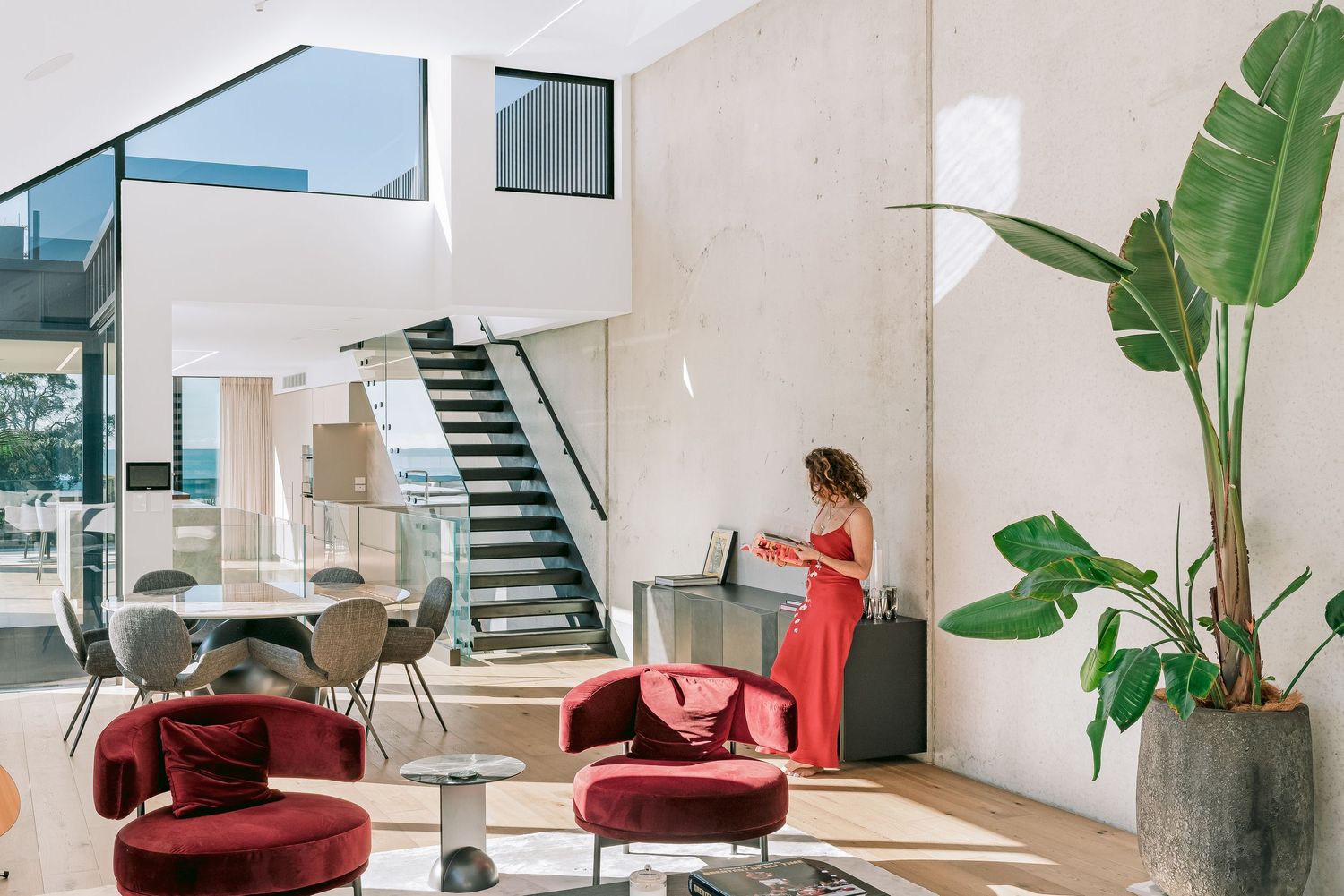 Stylish open concept living area with red armchairs, large houseplant and modern black staircase.