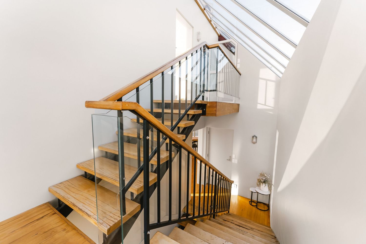 Modern wooden staircase with black metal railings and wooden handrail illuminated by skylight windows.