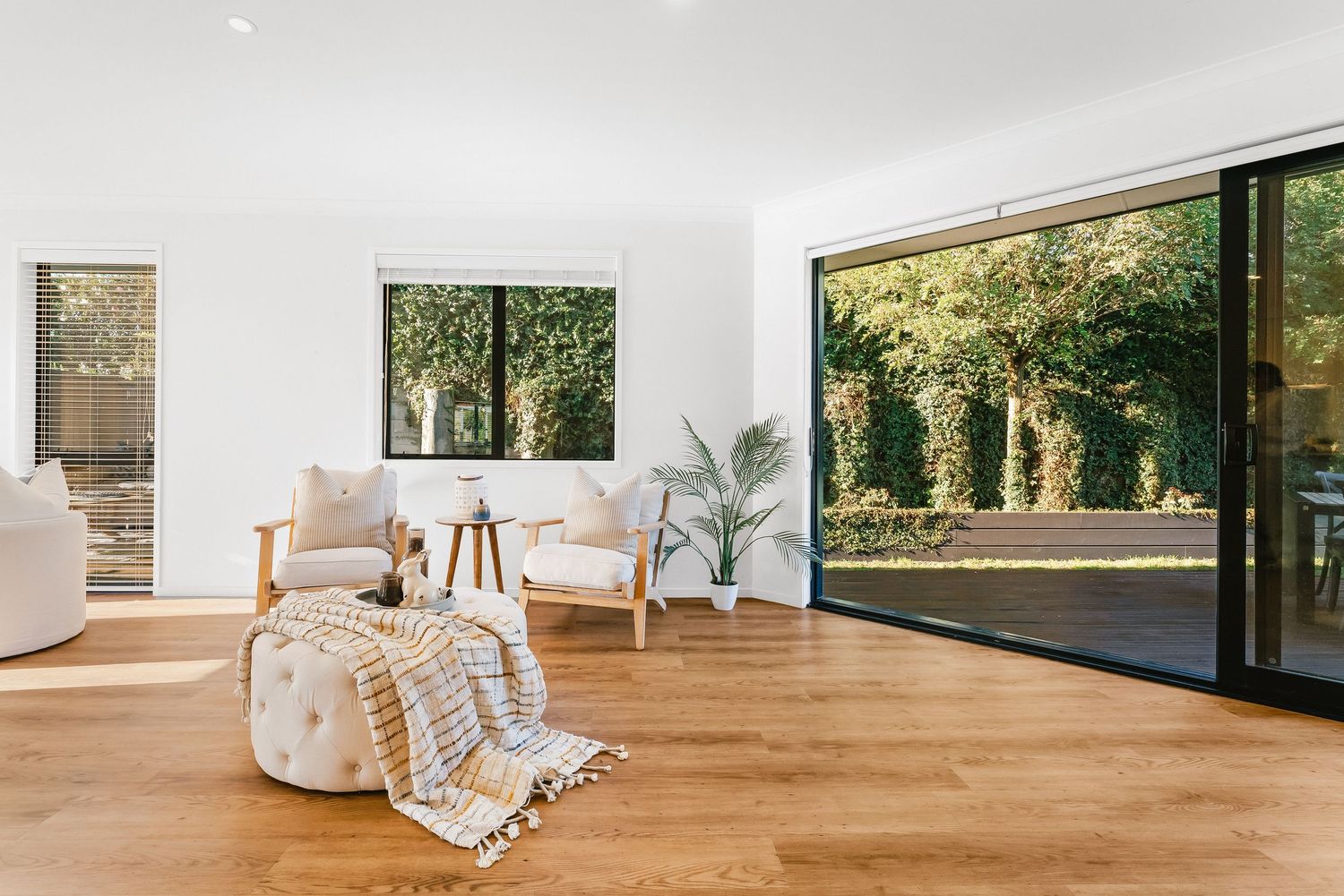 Modern living room with large windows, hardwood floors, white walls and cozy seating overlooking a lush garden view.