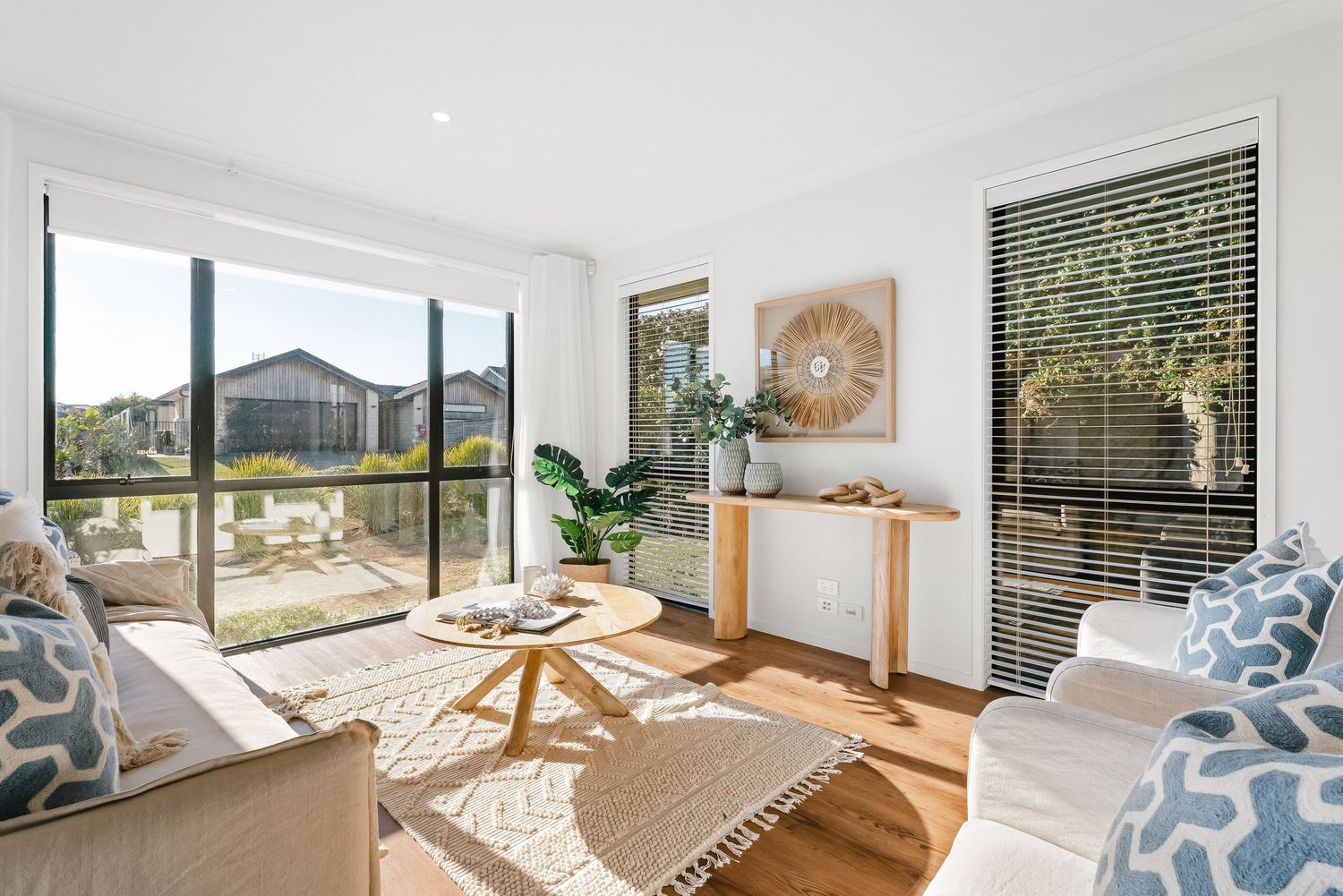 Modern coastal living room with natural light, beige sofa, wooden accents and panoramic windows overlooking mountain views.