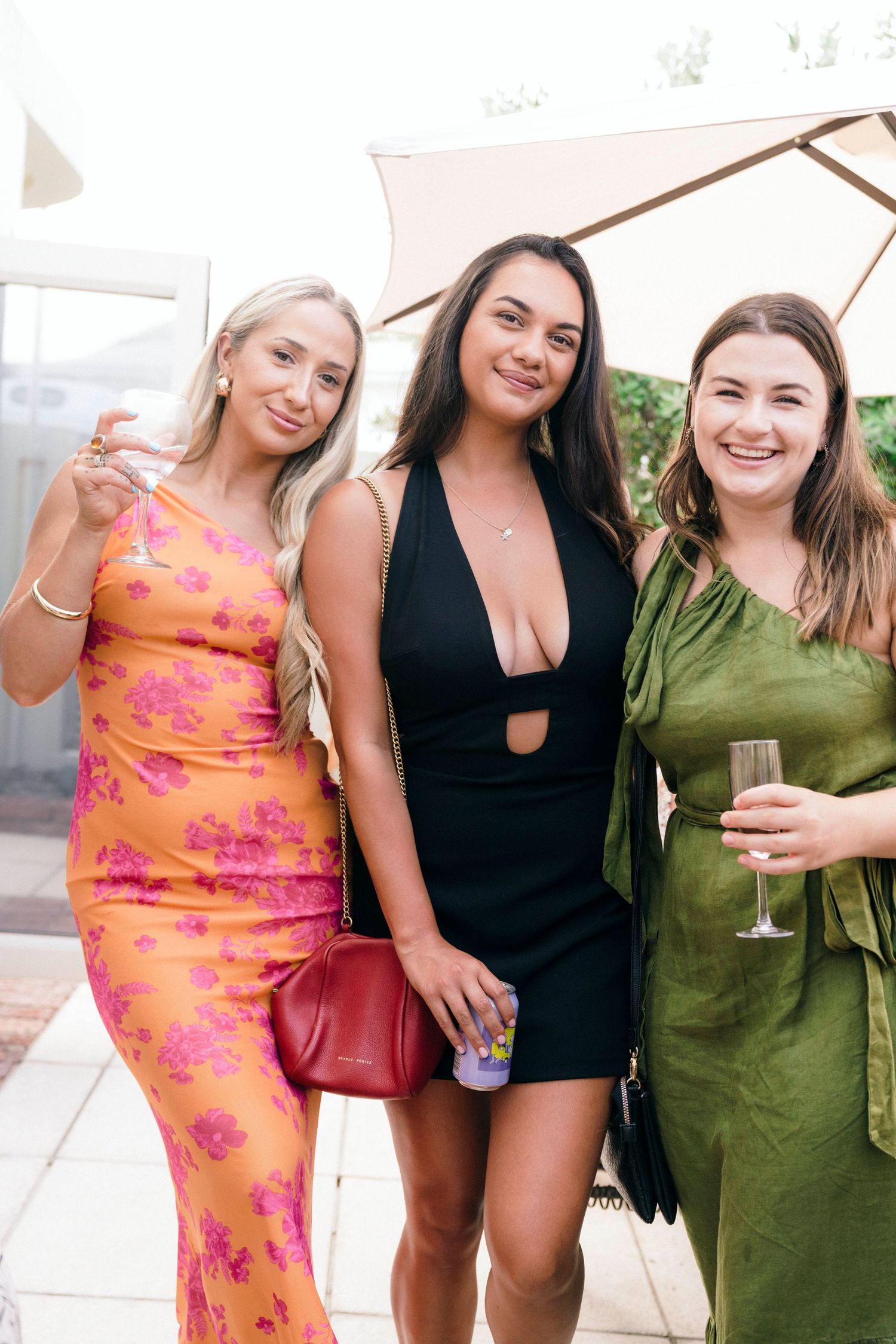 Three friends pose together at an outdoor event wearing colorful dresses.