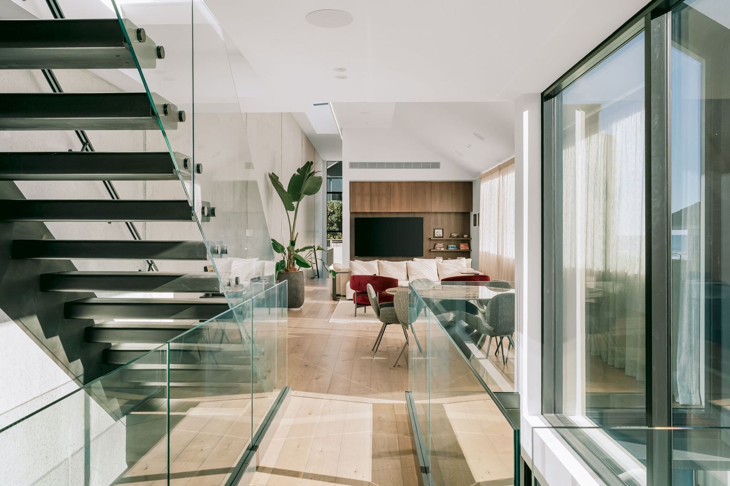 Modern open-concept interior with floating glass staircase and floor-to-ceiling windows.