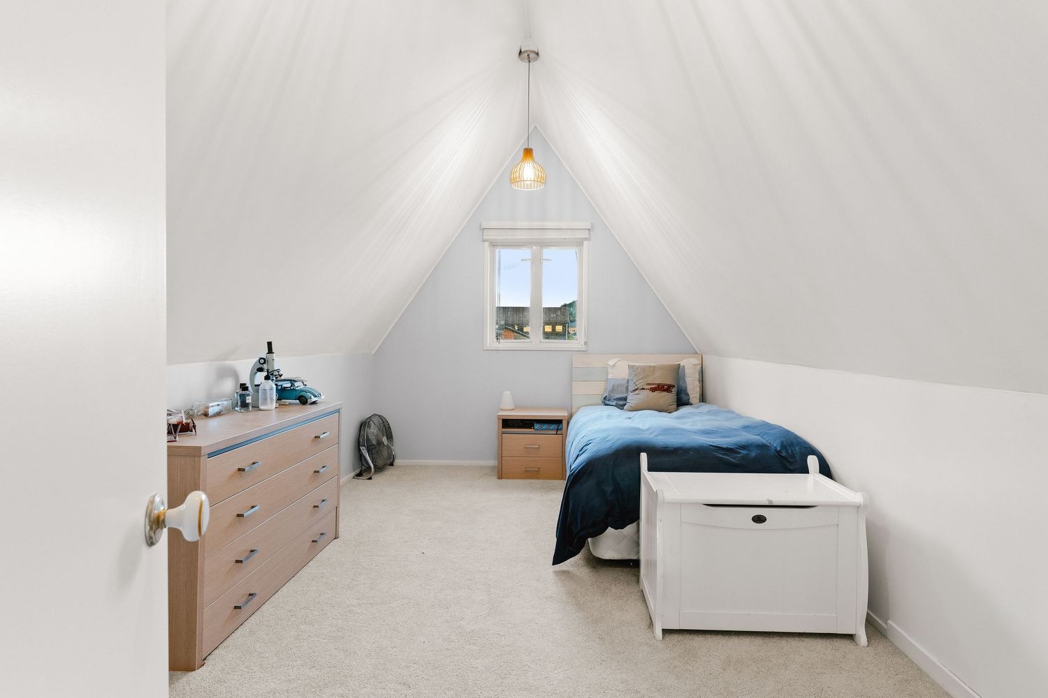 Spacious white attic room with sloped ceiling and minimal furniture.