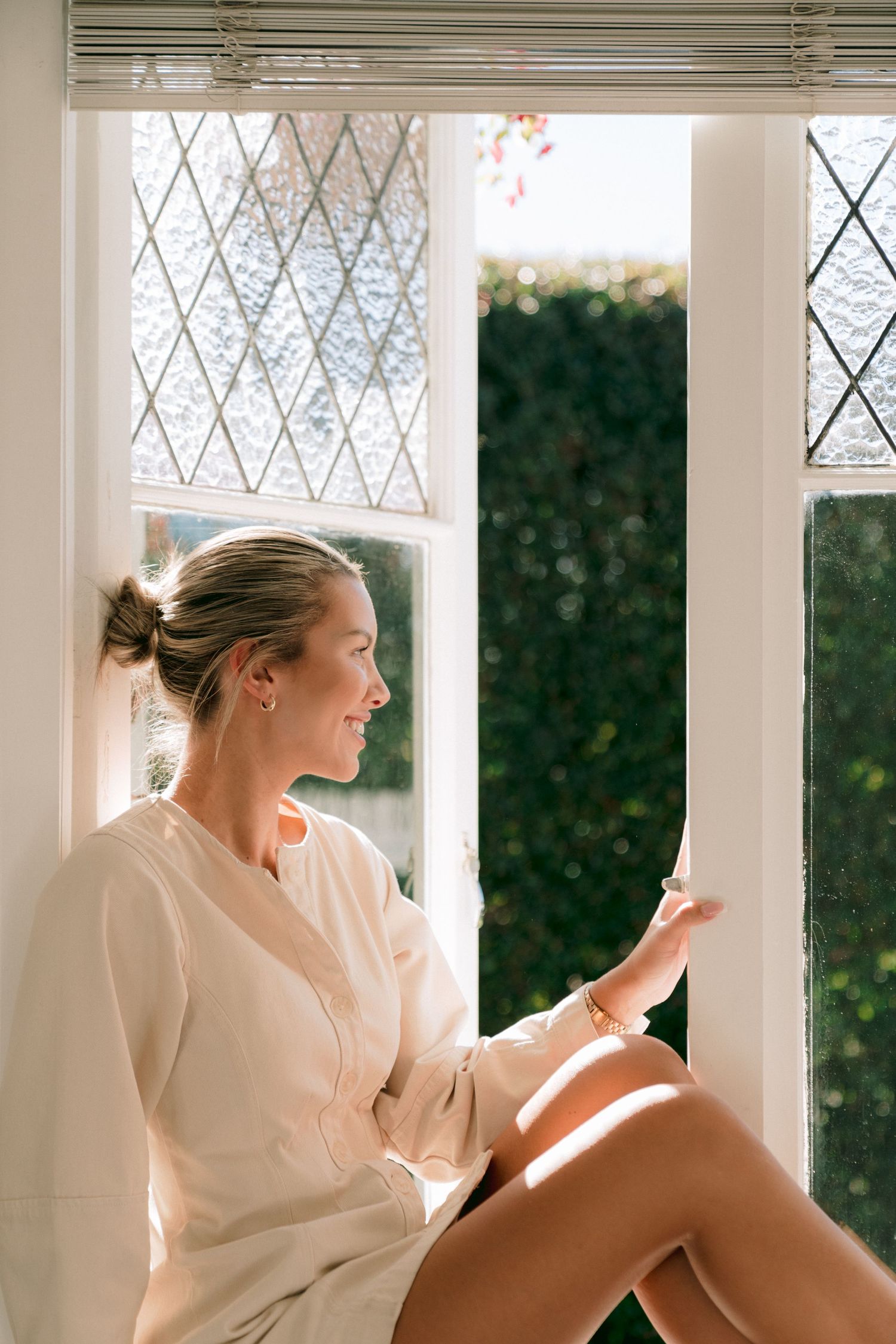 A person in white lounges contemplatively by a row of vintage windows with diamond panes.