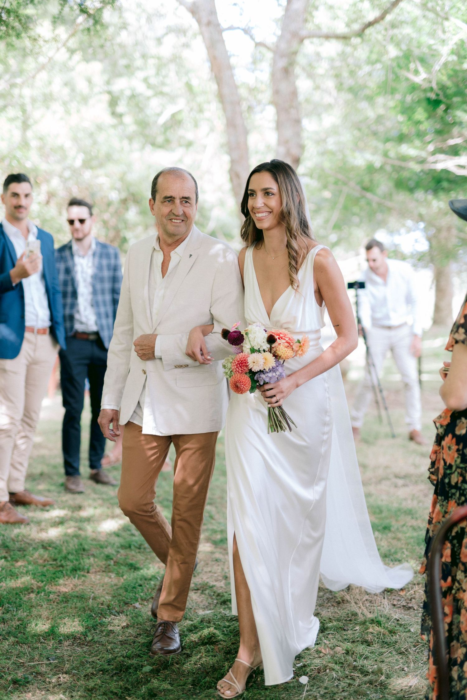 Wedding guests mingle outdoors in a casual garden setting with people wearing light summer attire.