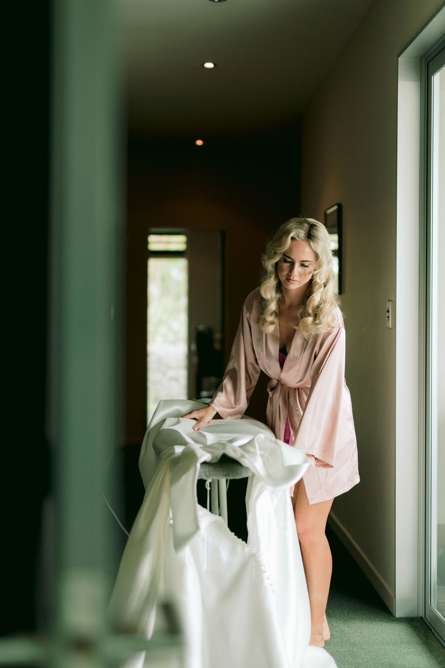 Wedding dress being prepared in a modern hallway with natural lighting.
