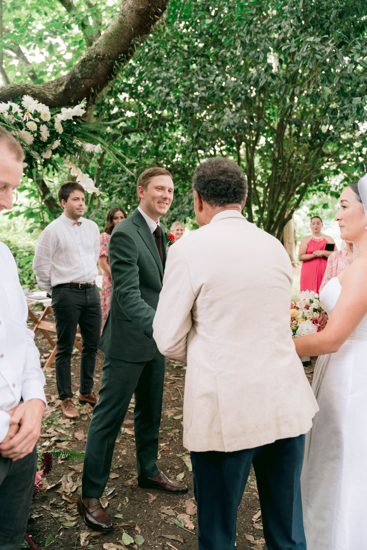 A small gathering of wedding attendees converse during an outdoor forest ceremony.