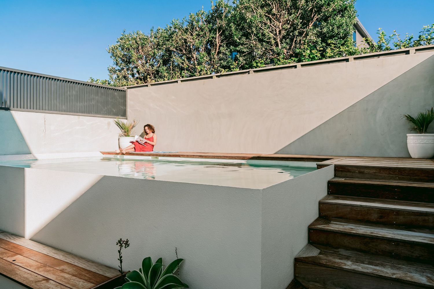 A contemporary rooftop deck space with clean white walls and wooden flooring overlooking a sunny poolside area.