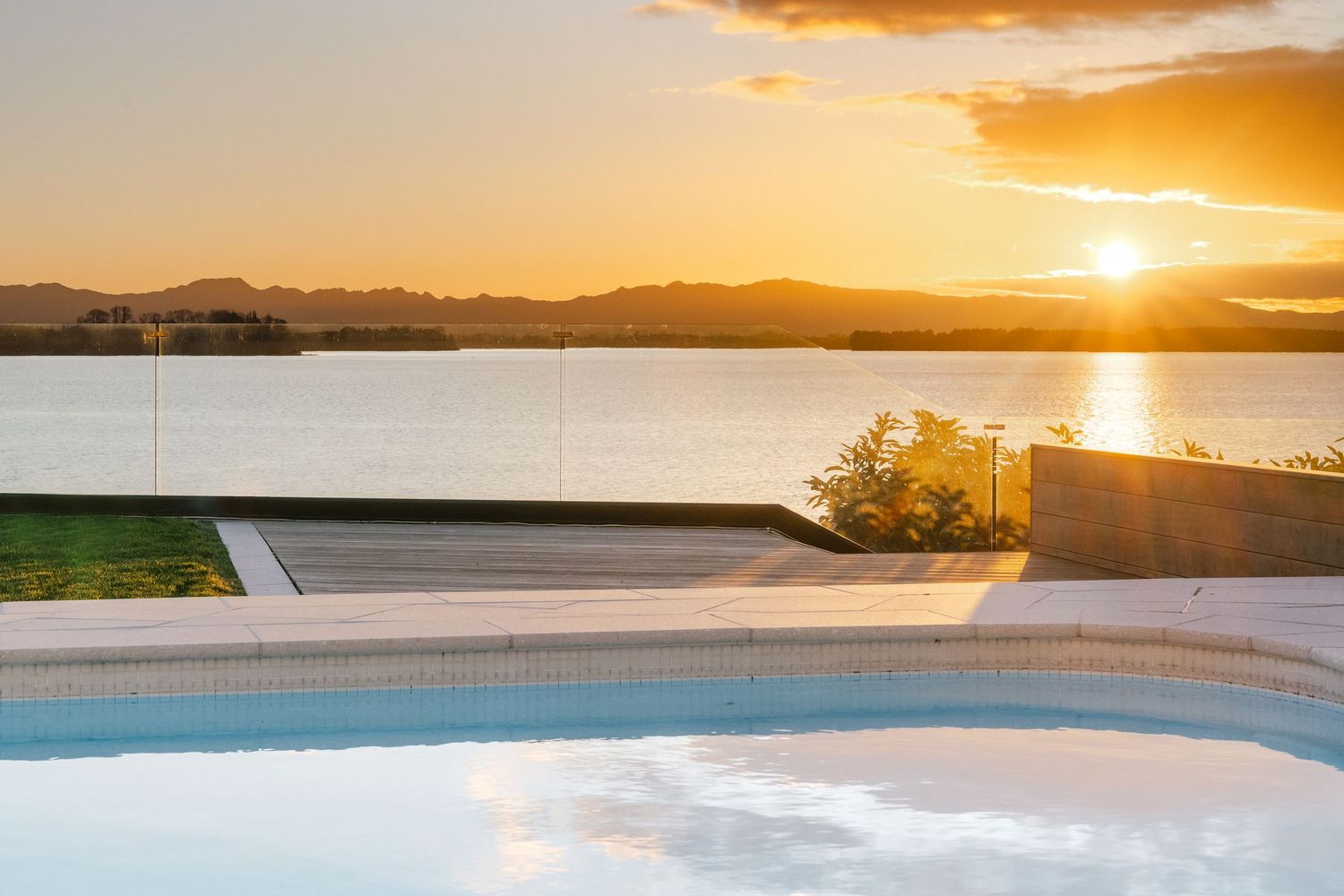 Stunning sunset view over a lake with mountains and infinity pool in the foreground.