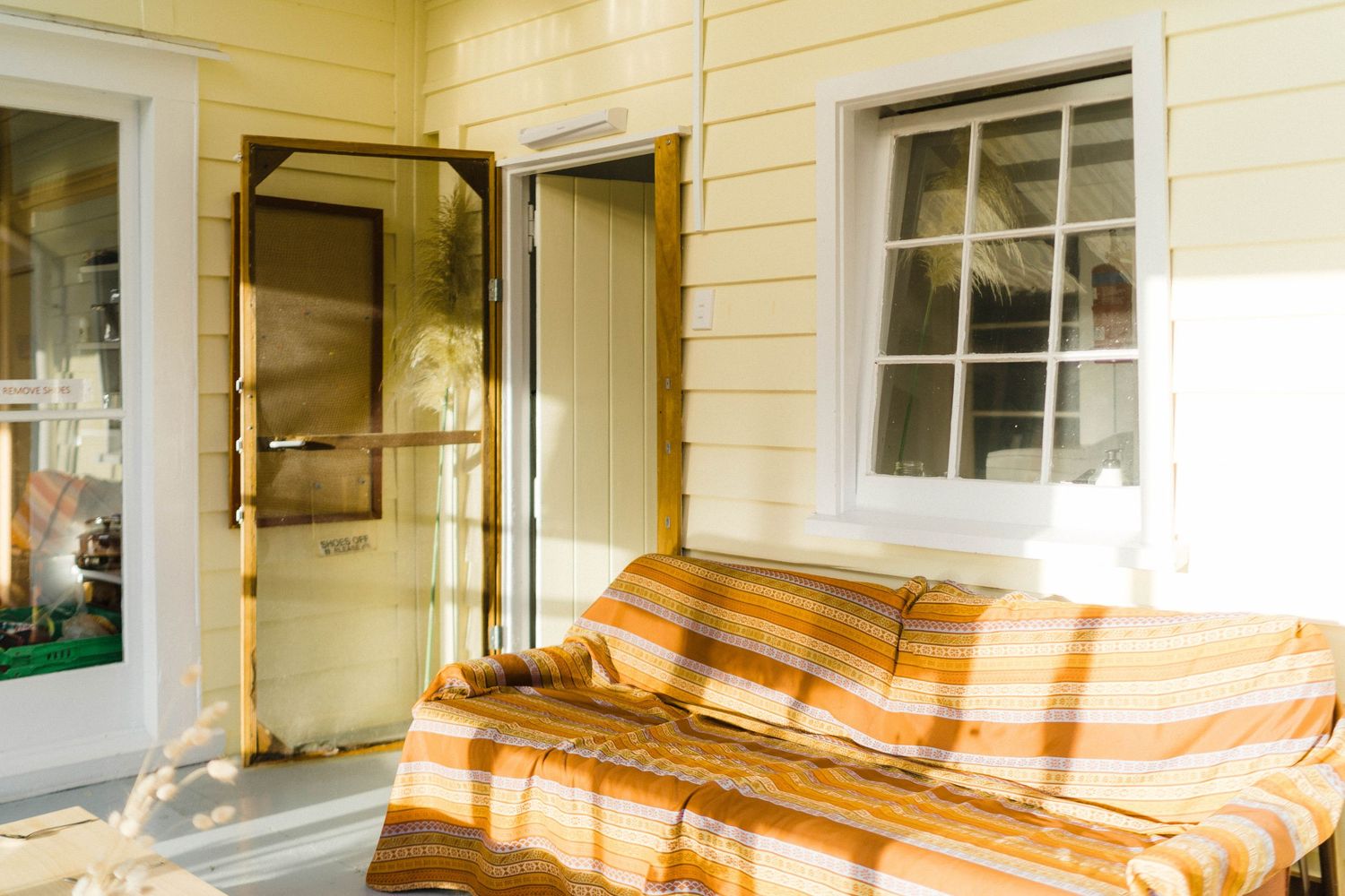 Yellow house porch with orange striped couch and white window frames.