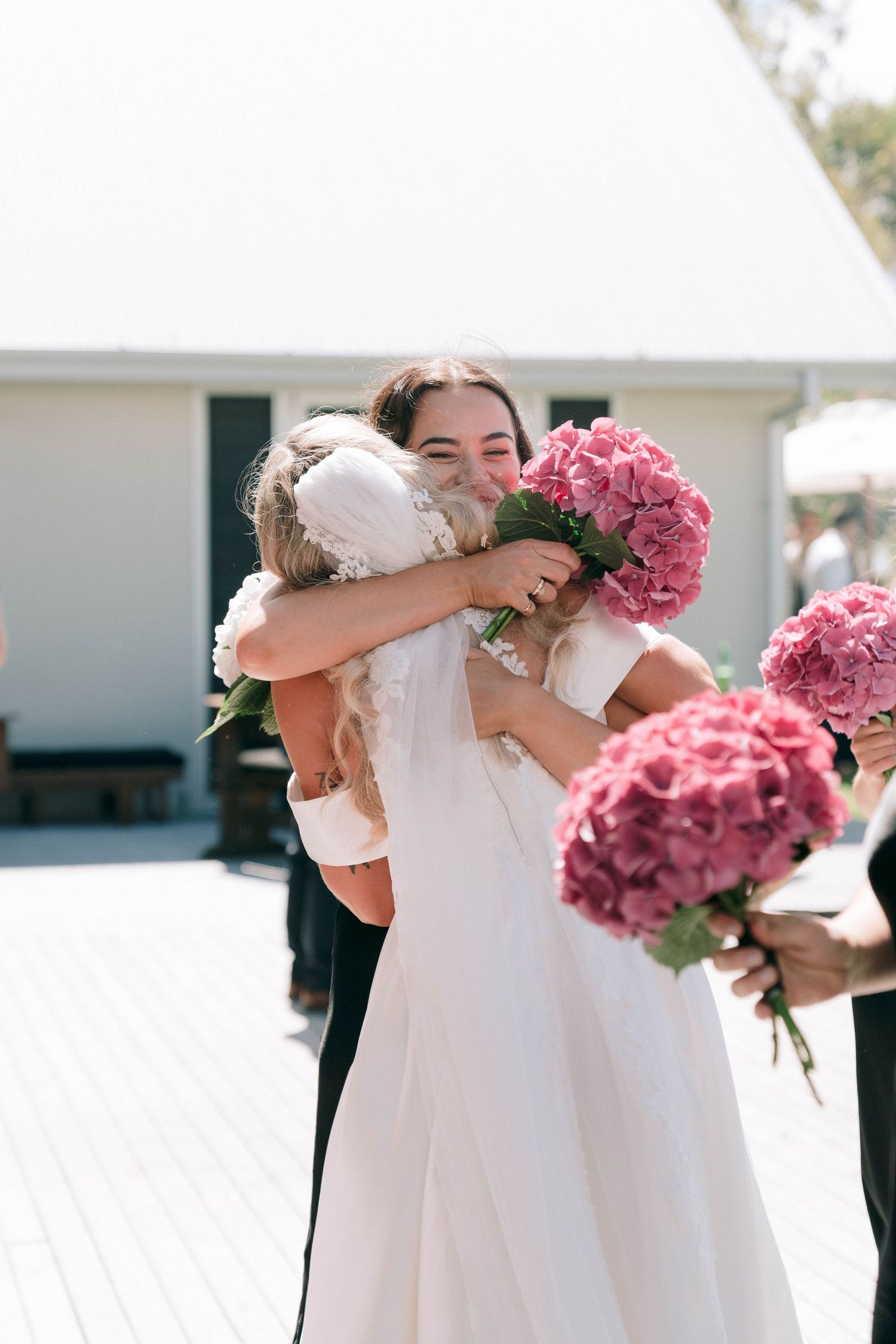 Wedding party members share emotional embraces while holding pink hydrangea bouquets.