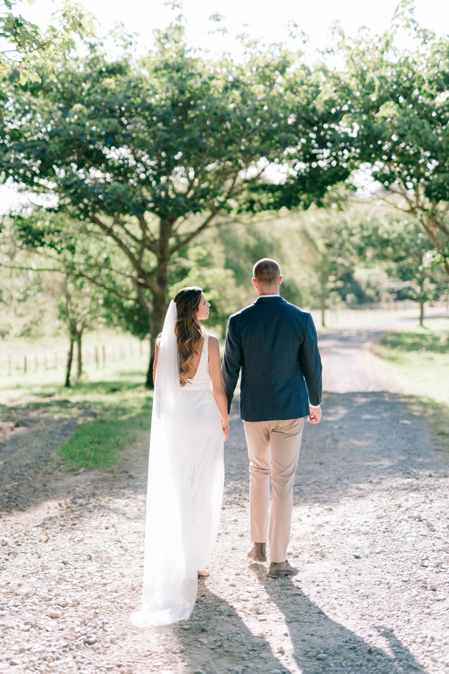 Newlywed couple walking down a tree-lined path in wedding attire.