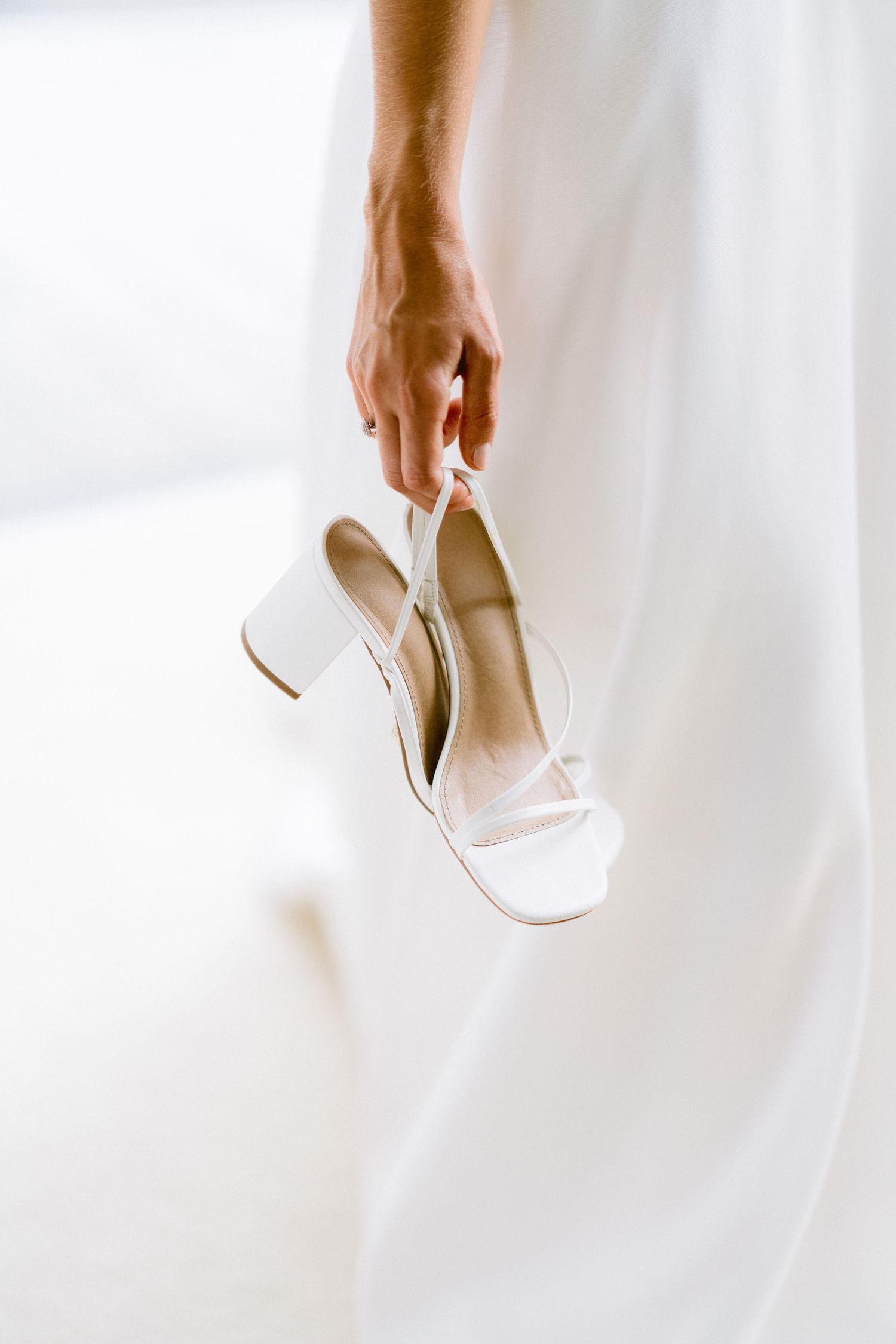 White bridal heels being held against a soft white background.