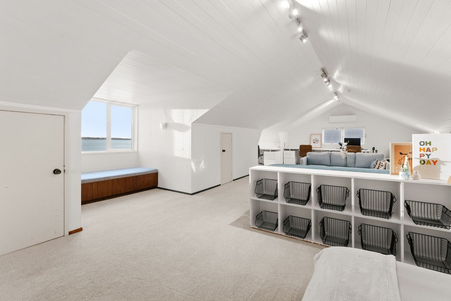 Spacious attic storage room with organized bins, track lighting, and sloped white ceiling.