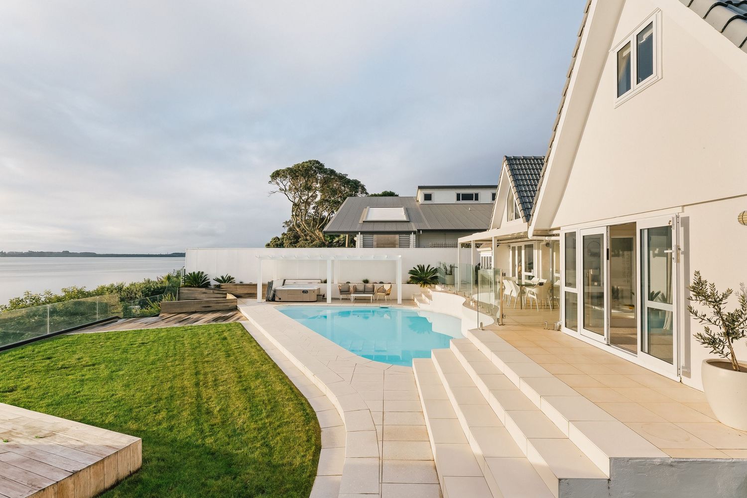 Modern waterfront home with infinity pool and expansive lawn overlooking the ocean.