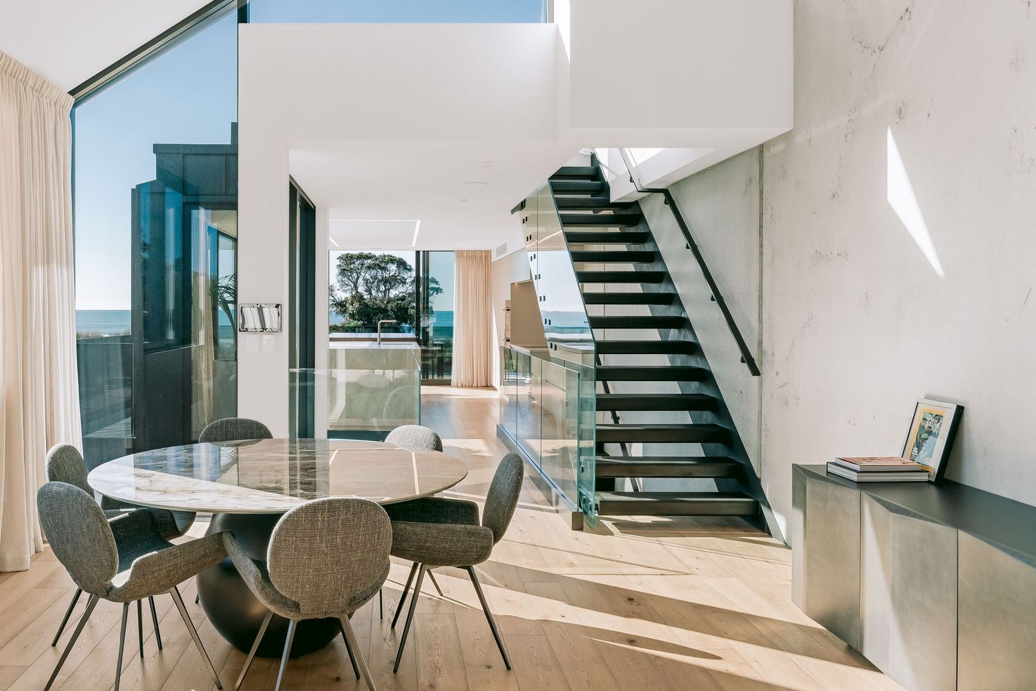 Modern minimalist loft apartment interior featuring white walls, gray upholstered chairs and sleek glass accents.