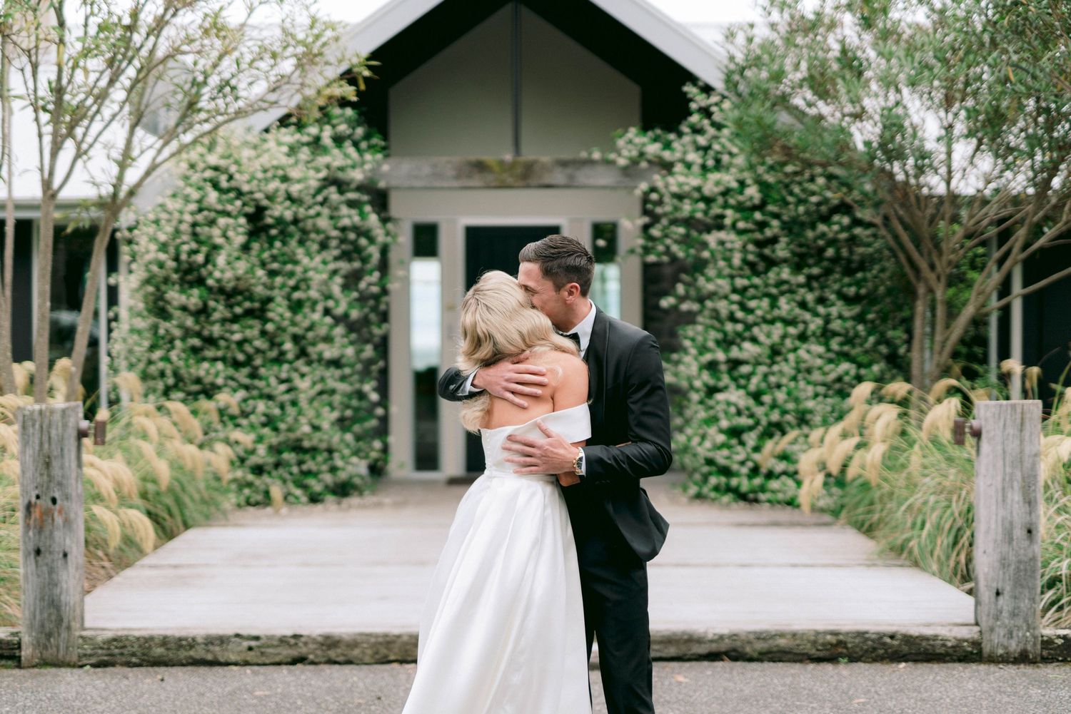 A romantic embrace in front of a chapel covered in climbing vines and greenery.