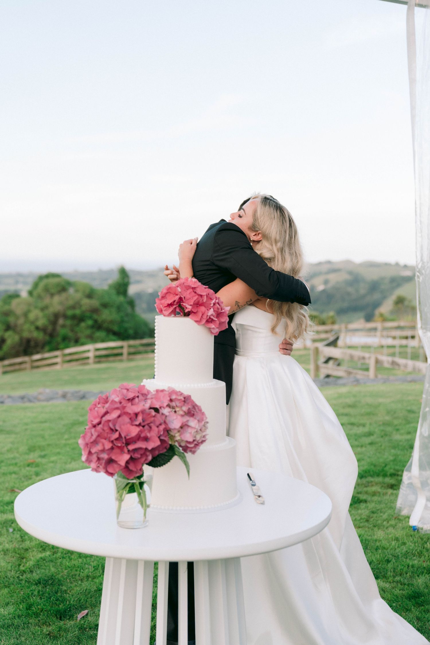 Romantic moment by a round table decorated with pink hydrangeas at an outdoor wedding.