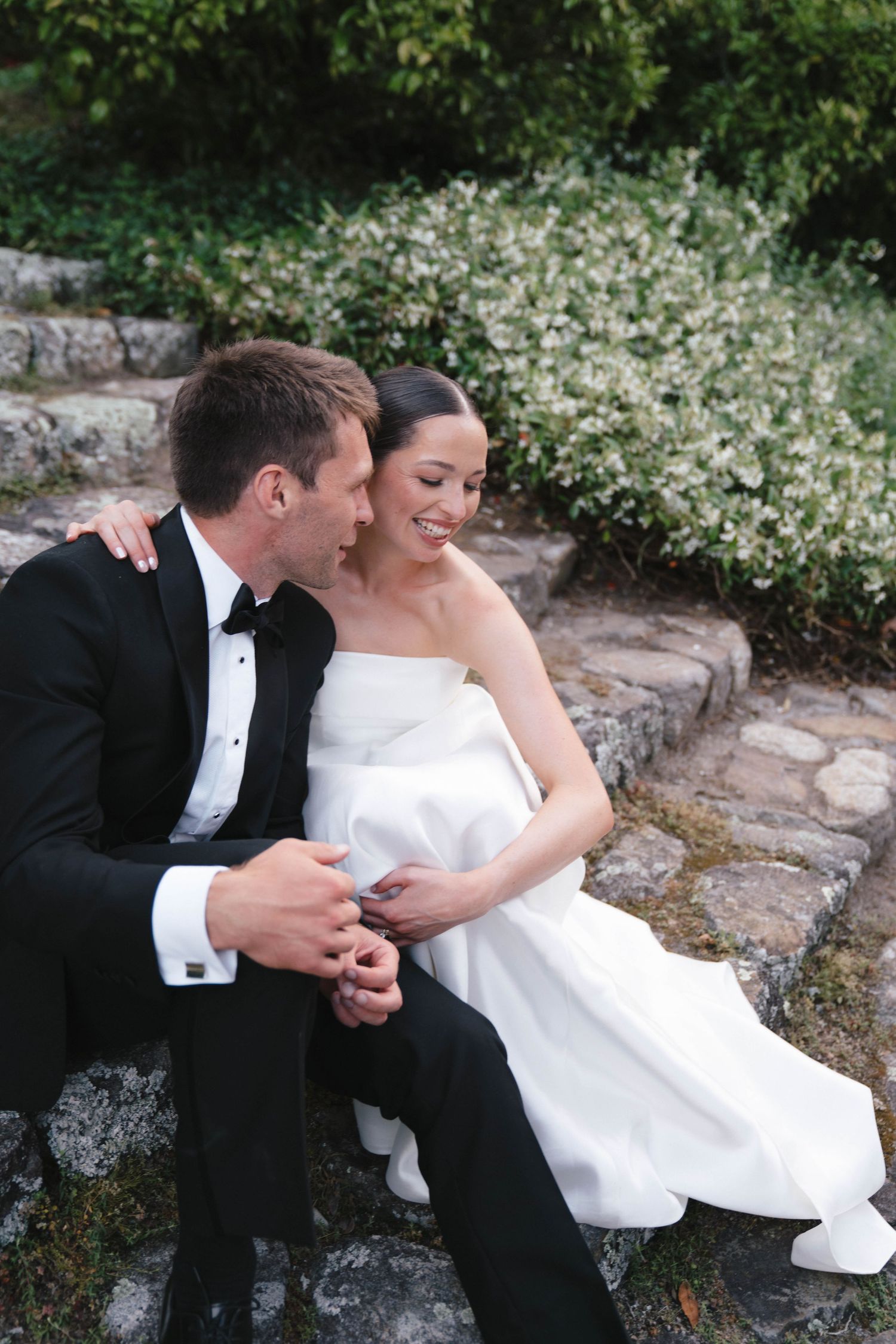 Couple in wedding attire sharing an intimate moment on stone steps.