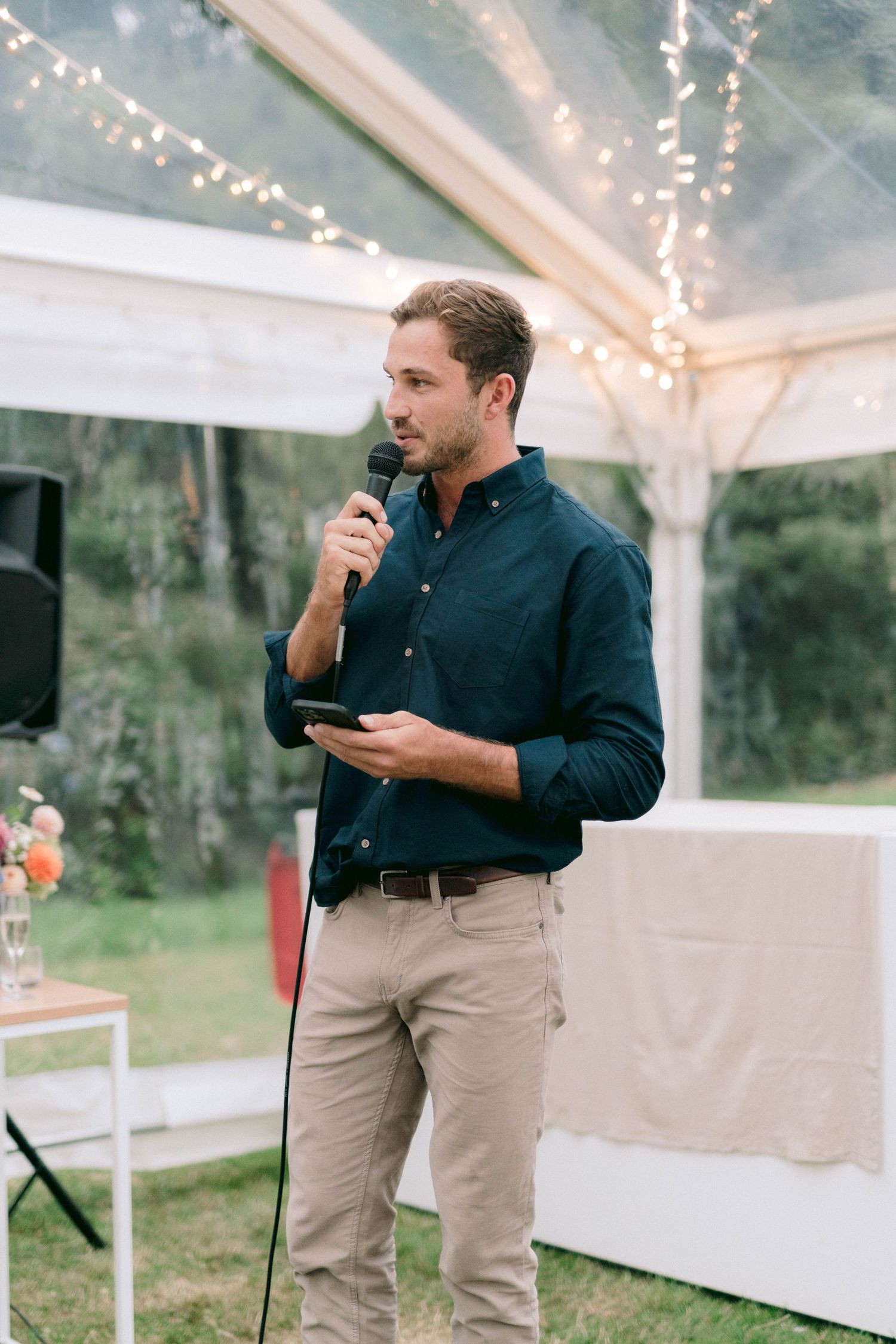 Speaker giving a heartfelt speech during an outdoor reception under string lights.