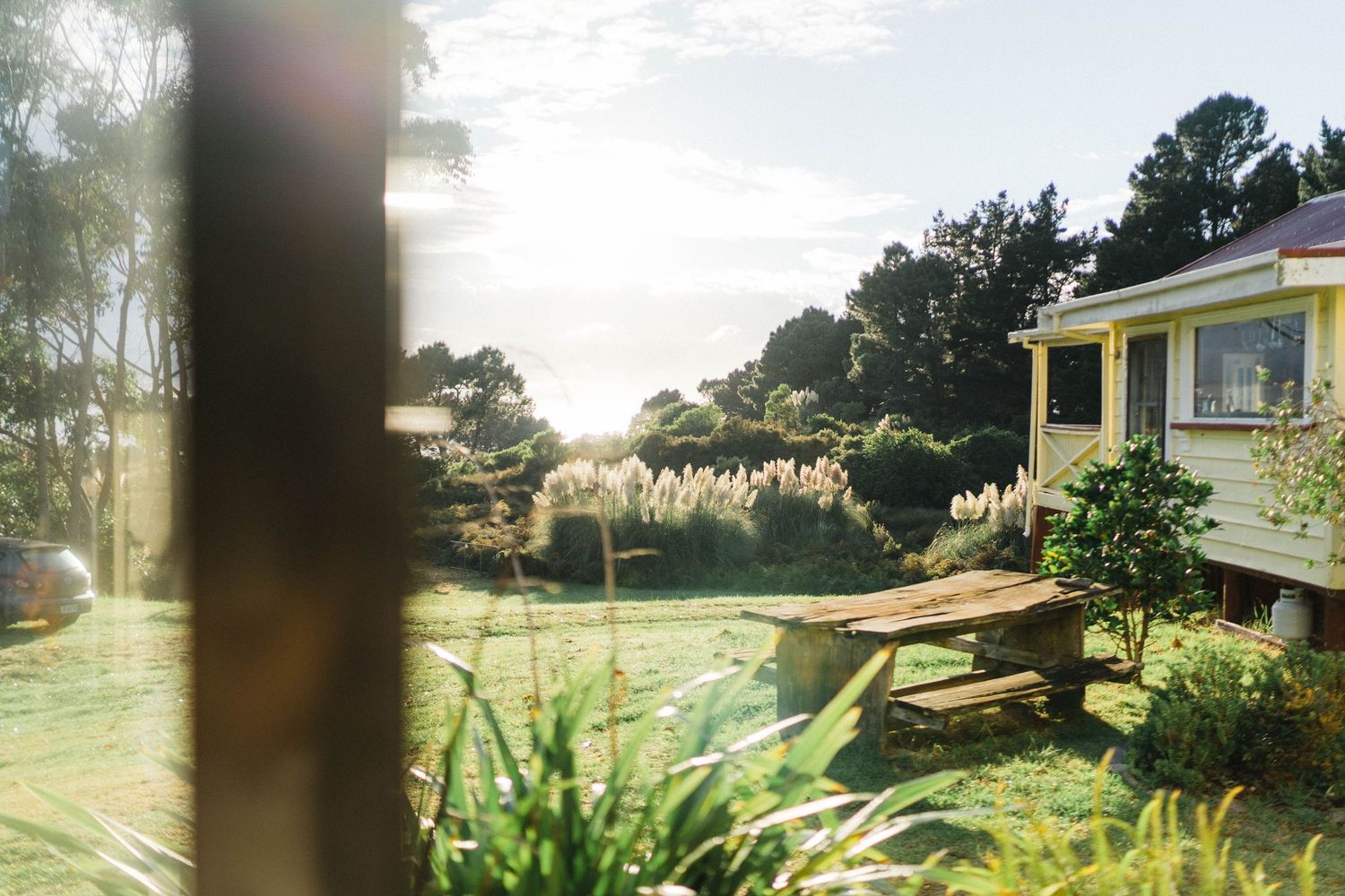 Yellow beach house exterior with trees and ocean view in soft golden light.