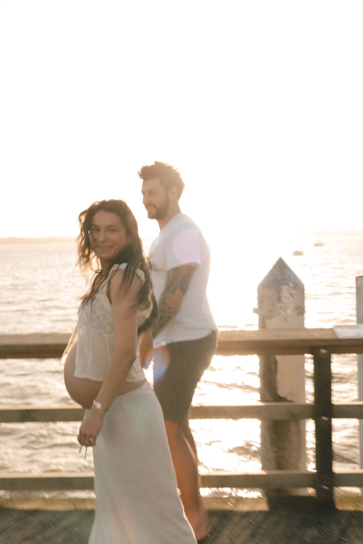 Couple enjoying a romantic sunset moment on a wooden pier overlooking the ocean.