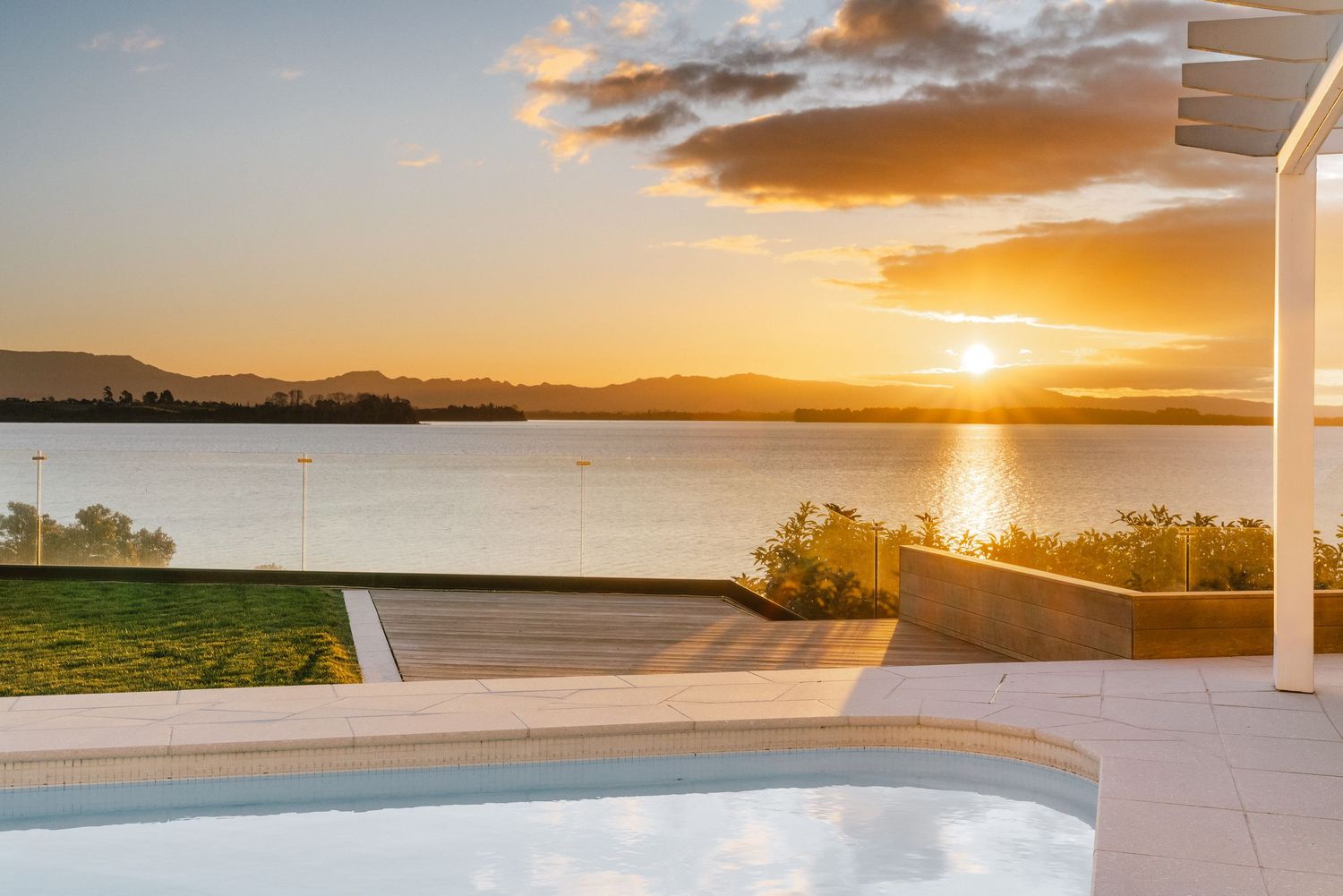 Stunning sunset view over water with orange sky and modern patio setting.