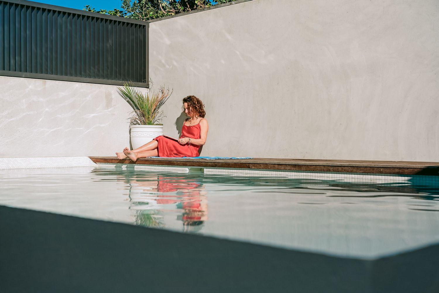 Woman relaxes on a luxurious pool deck with lounge chairs and white architectural walls in warm sunlight.