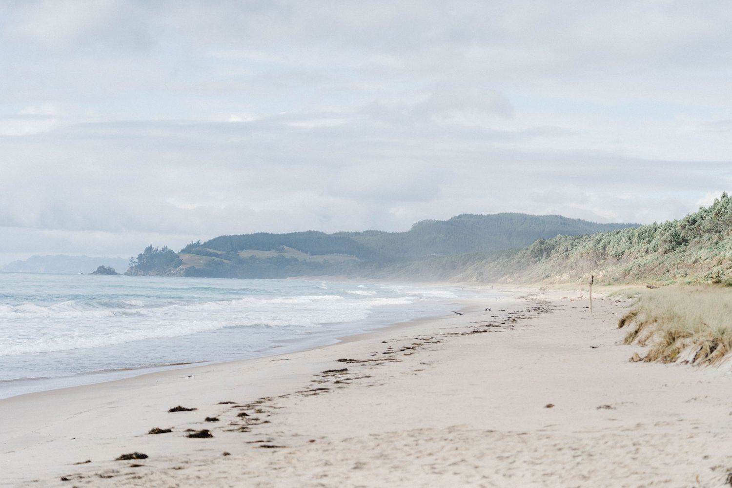 Serene coastal landscape with misty mountains and sandy beach stretching into the distance.