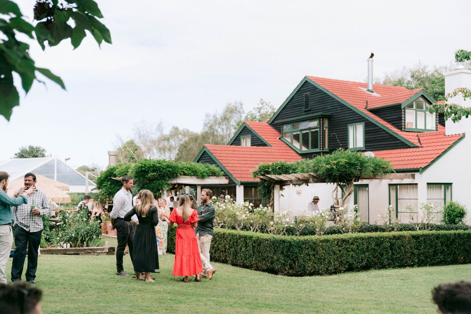 Guests gathered outside a charming house with red roofs and manicured hedges during a summer event.