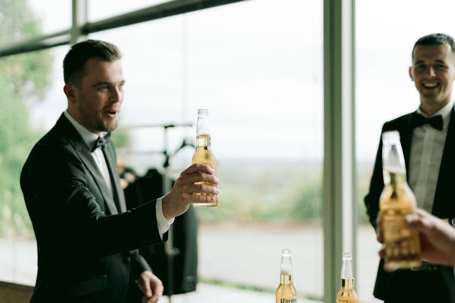 Wedding party members in formal attire toasting with bottles in a bright room.