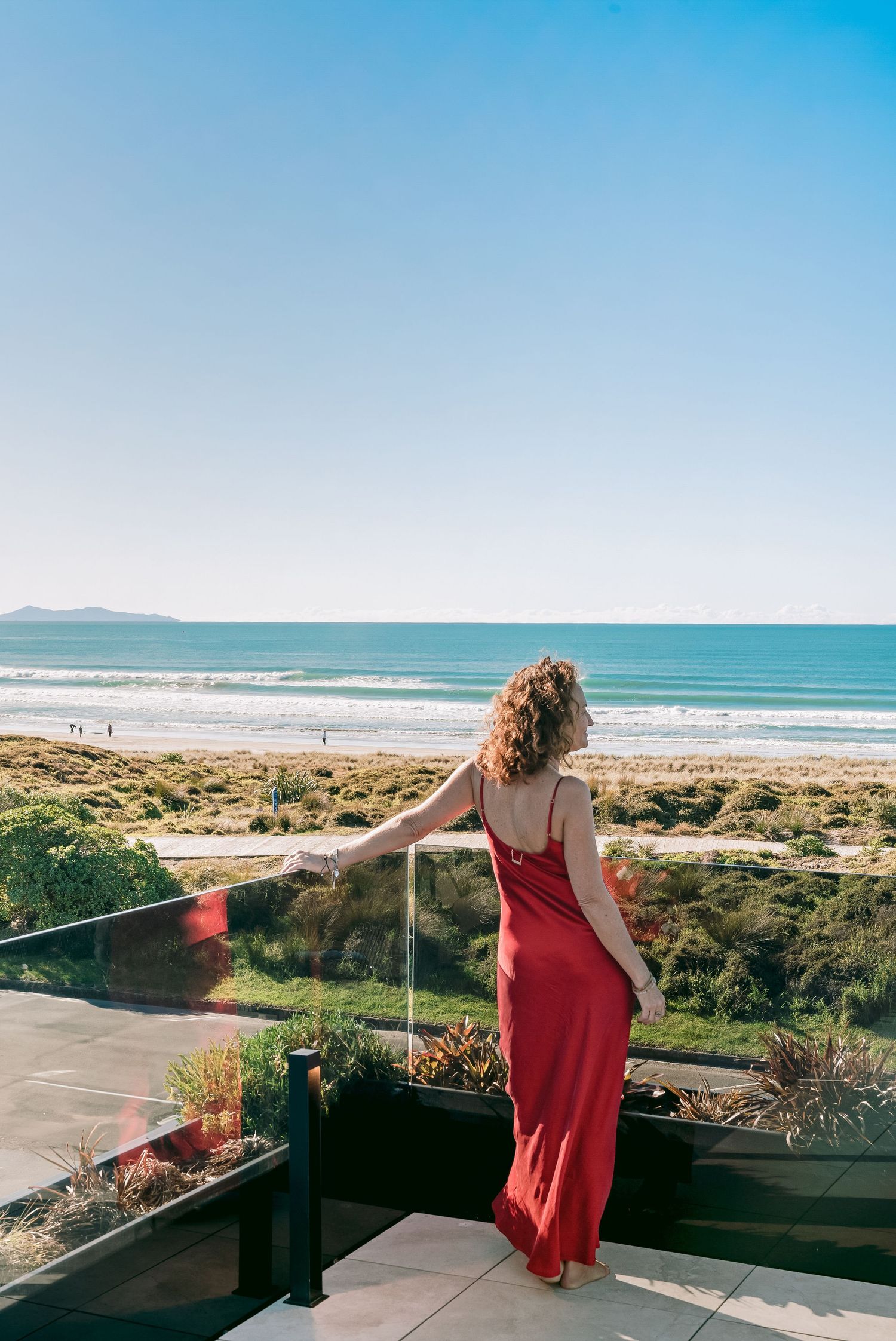 Scenic ocean view from a modern deck with glass railing overlooking sandy beach.