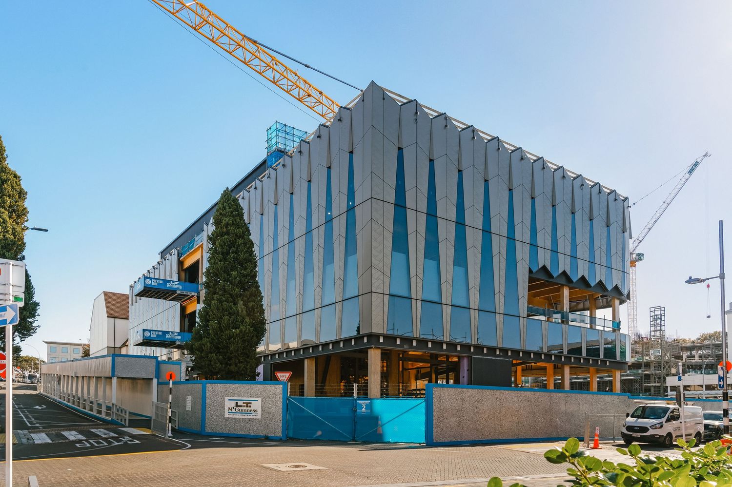 Modern office building under construction with glass panels and construction cranes visible in Auckland.