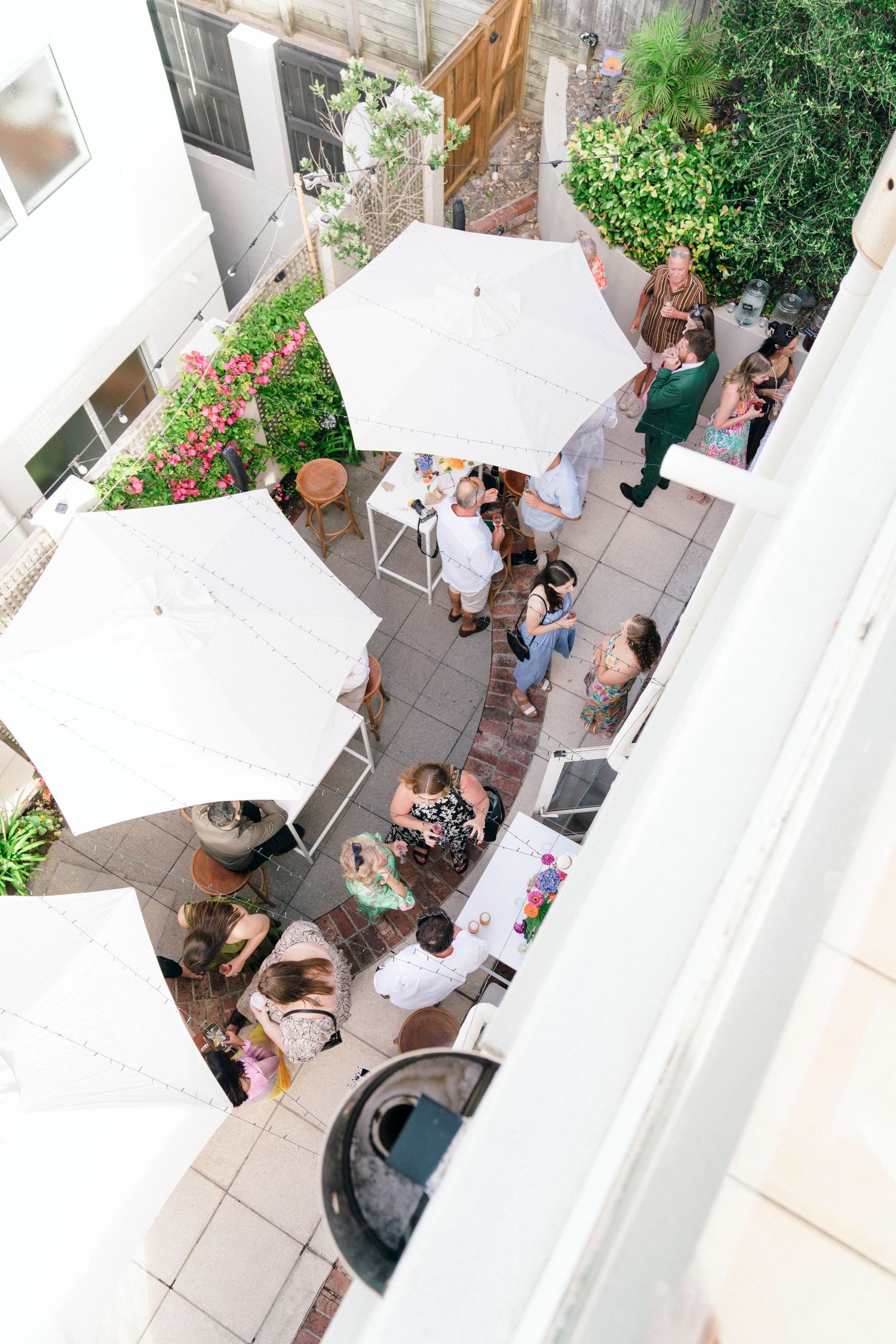 Aerial view of a courtyard patio with white umbrellas and guests gathered for an outdoor event.