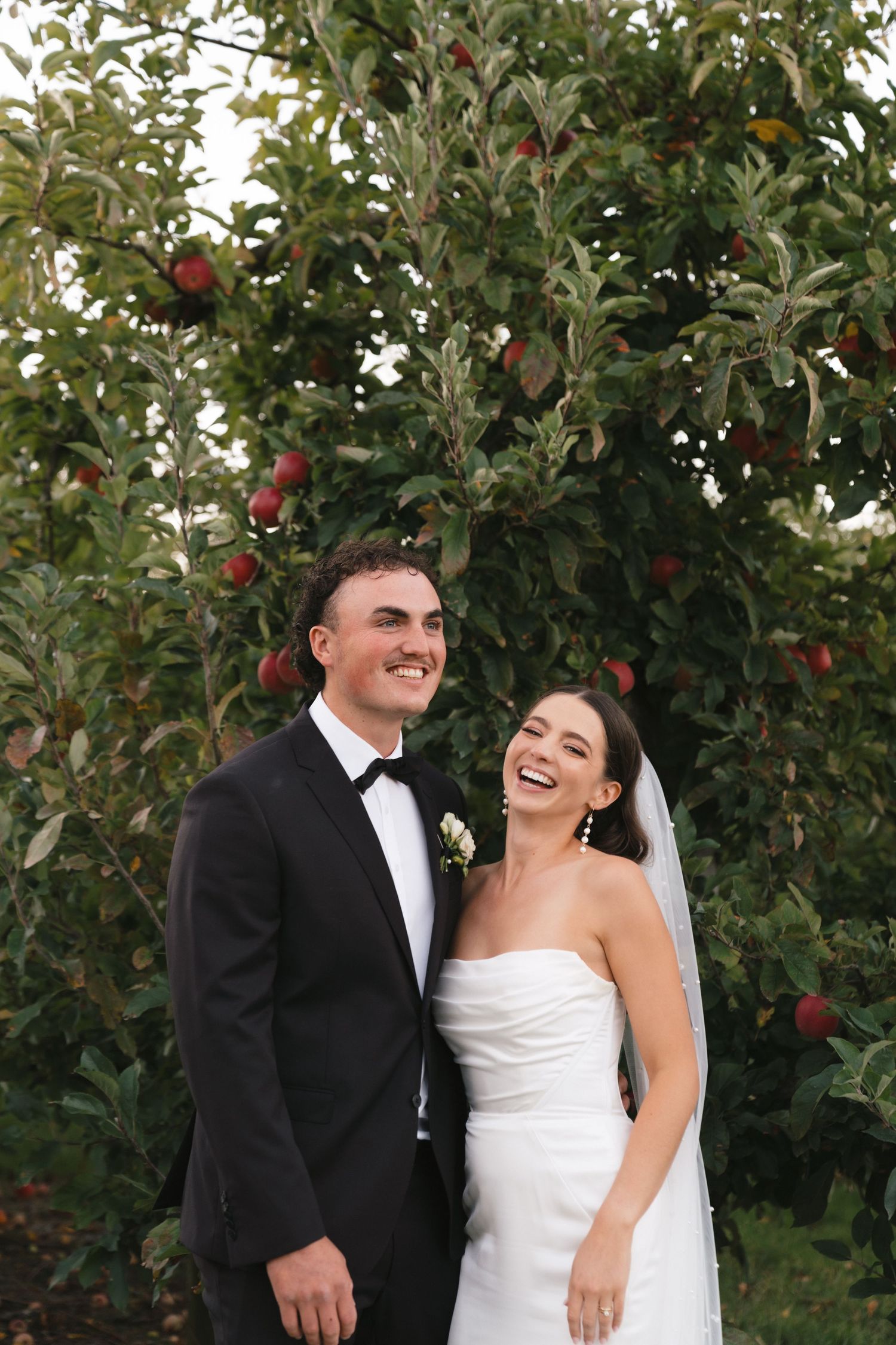 A joyful bride and groom share intimate moments in an apple orchard during their wedding photo session.