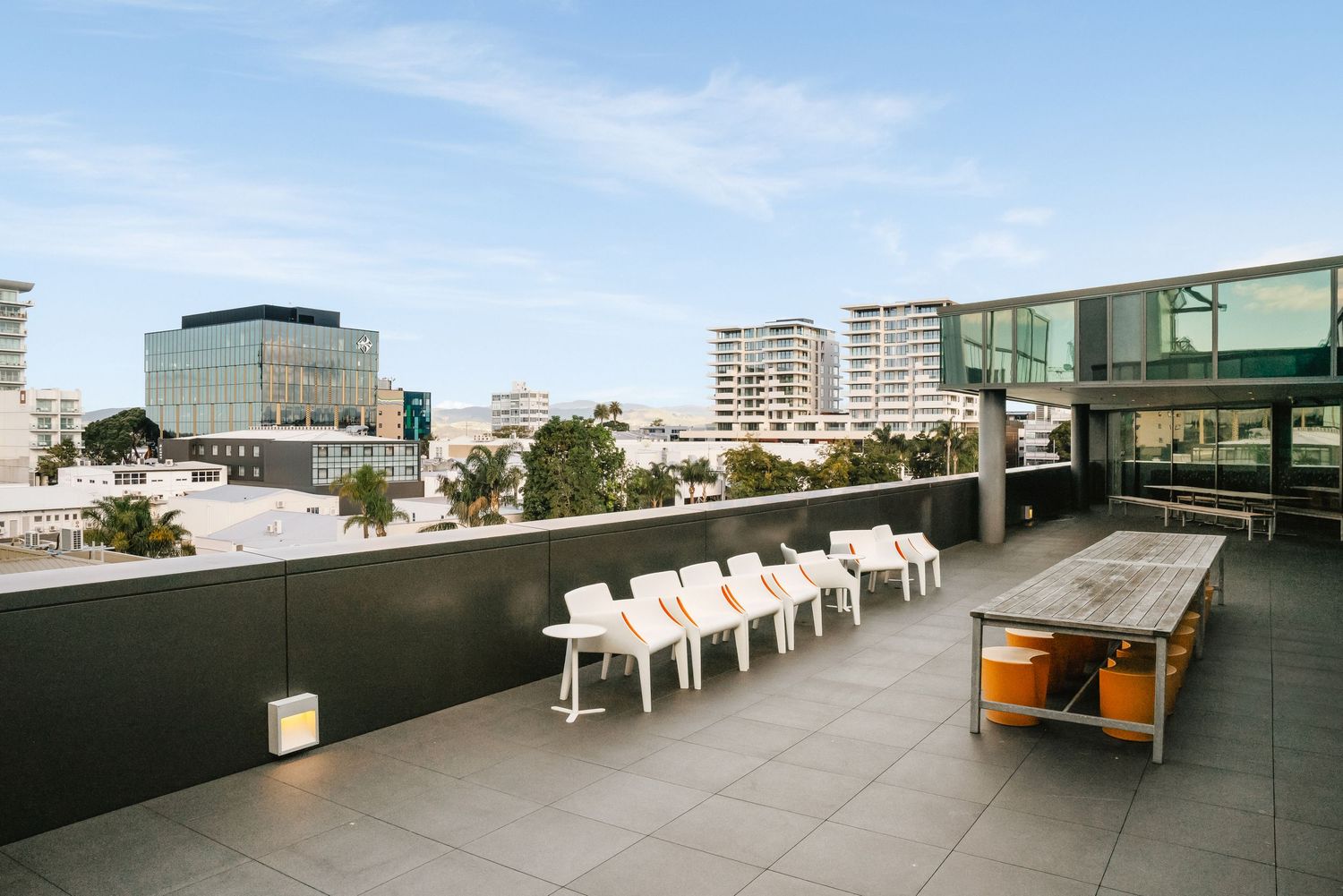 Modern rooftop terrace with white chairs and city skyline views featuring contemporary apartment buildings and amenities.