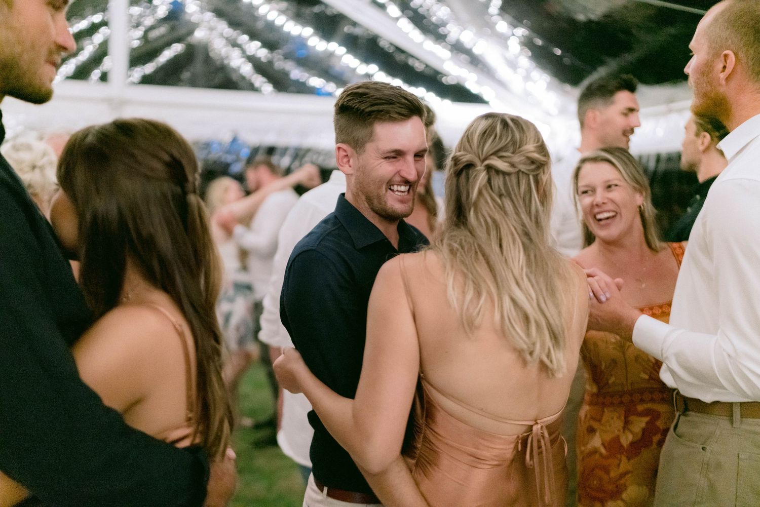 Guests dancing and celebrating at an evening wedding reception under a tent.