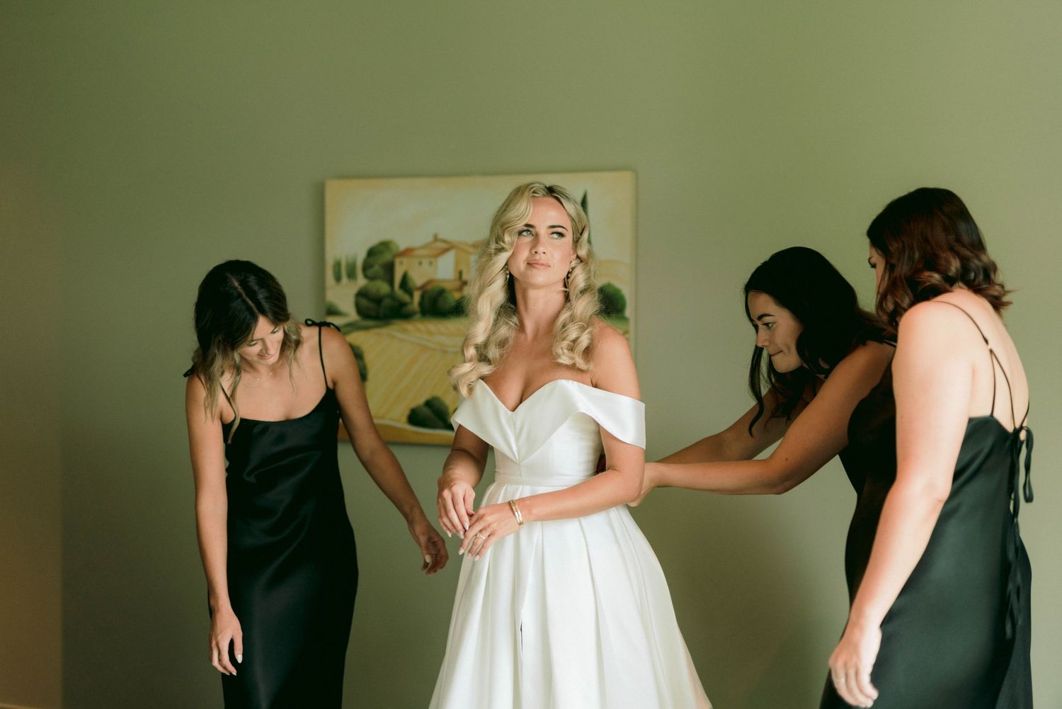 Wedding preparation scene with attendants helping with a white bridal gown.