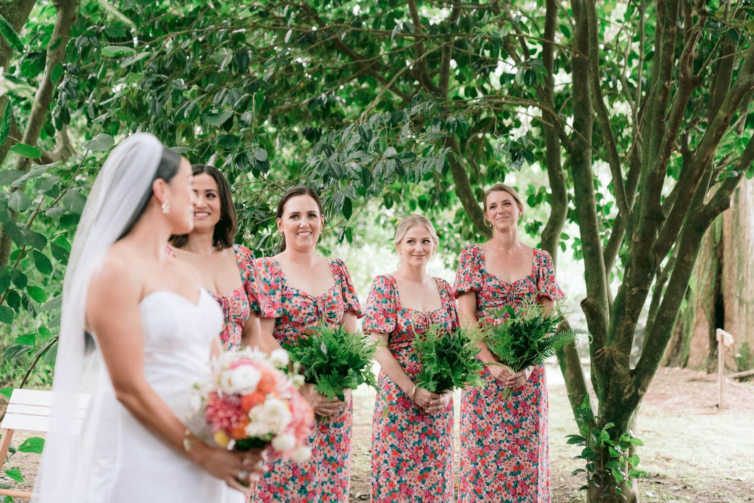Wedding party gathering under lush green trees in summer garden.