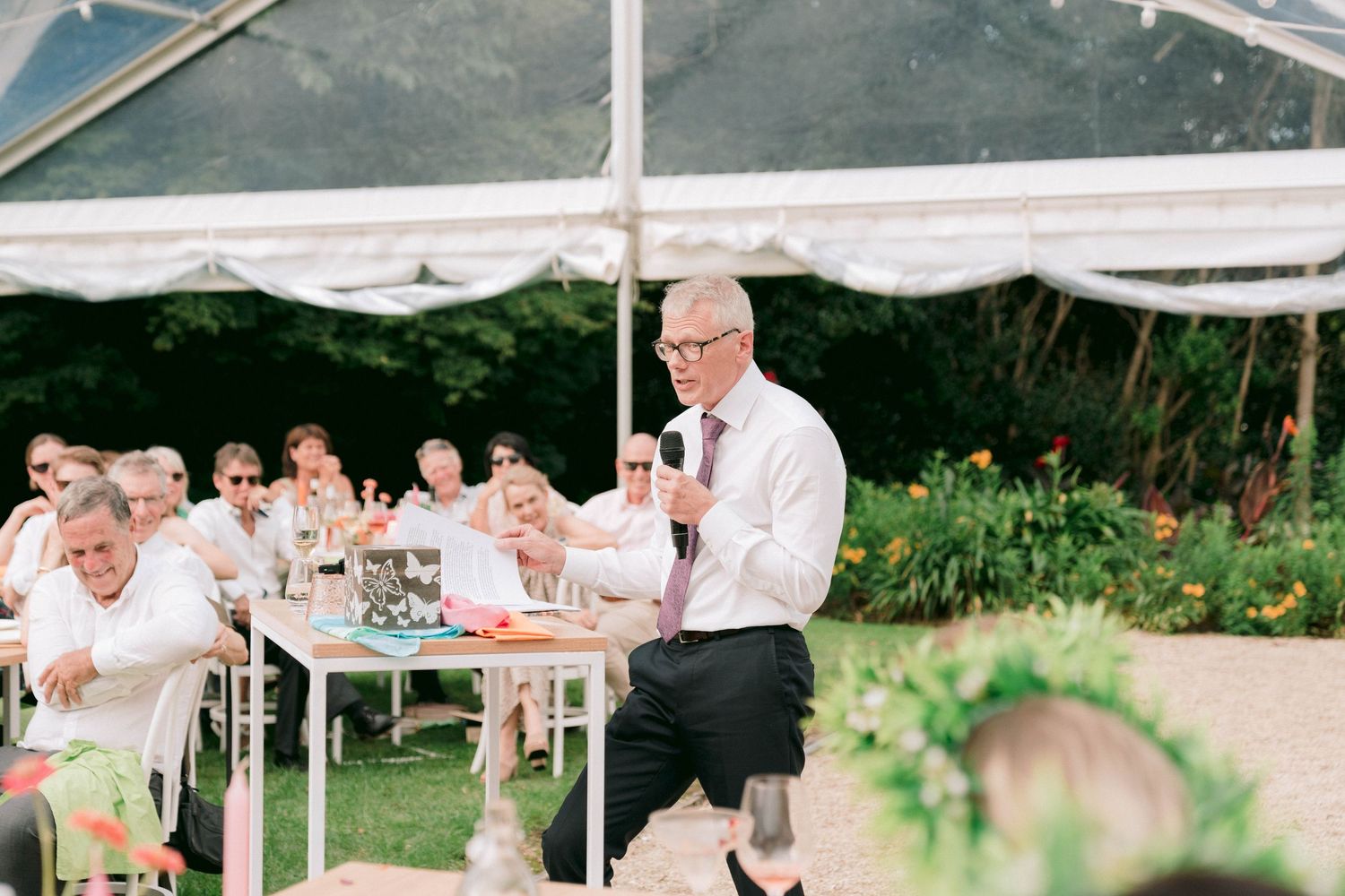 Guests seated under a white tent at an outdoor event.
