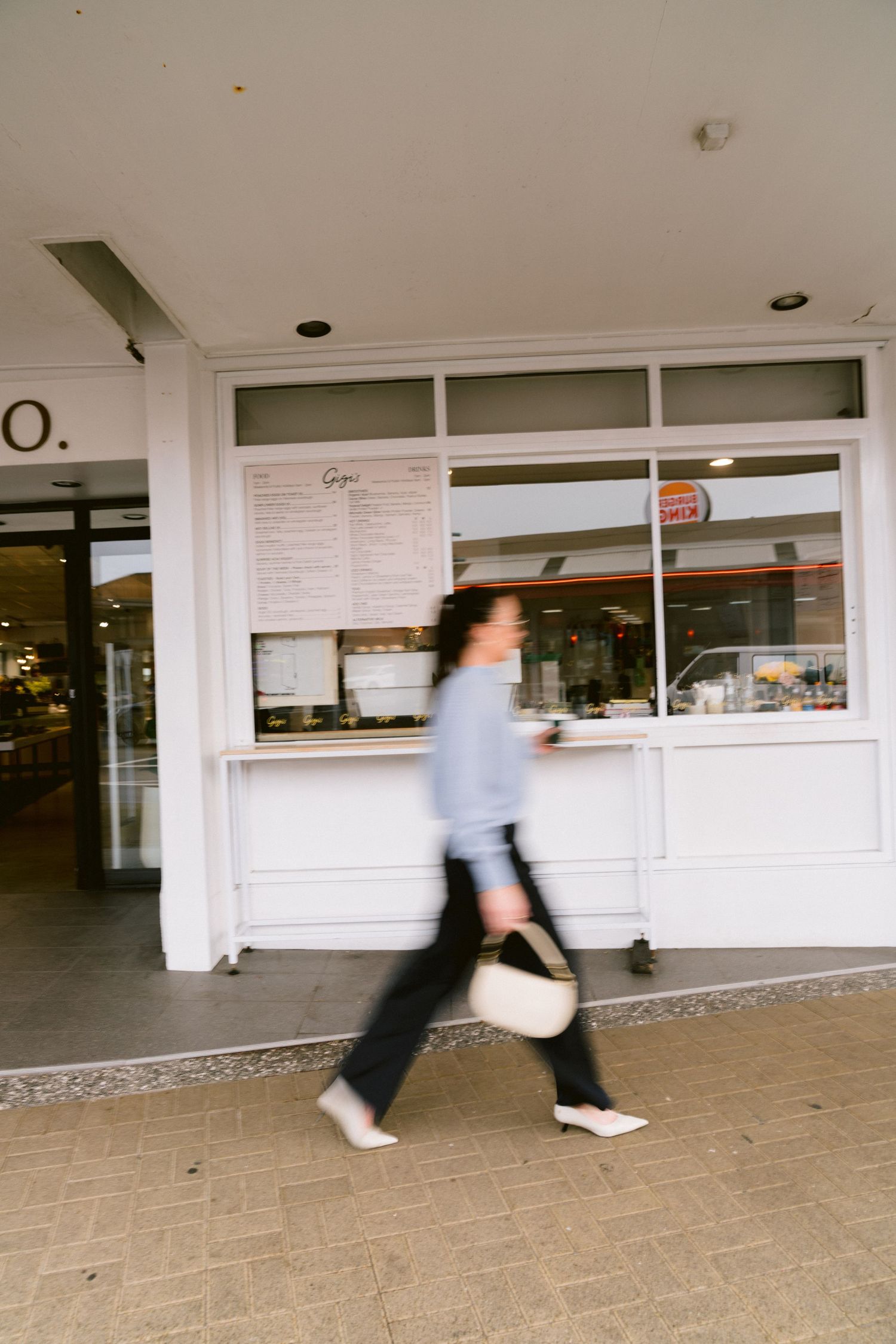 Blurred motion sequence of a person in blue shirt walking past a white service counter with windows at a retail location.